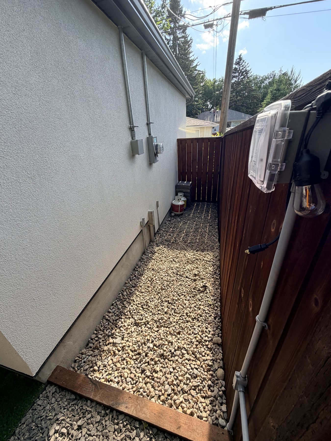 Exterior house wall with electrical conduits, gas tanks, and gravel path — 3505 41 Street SW, Calgary
