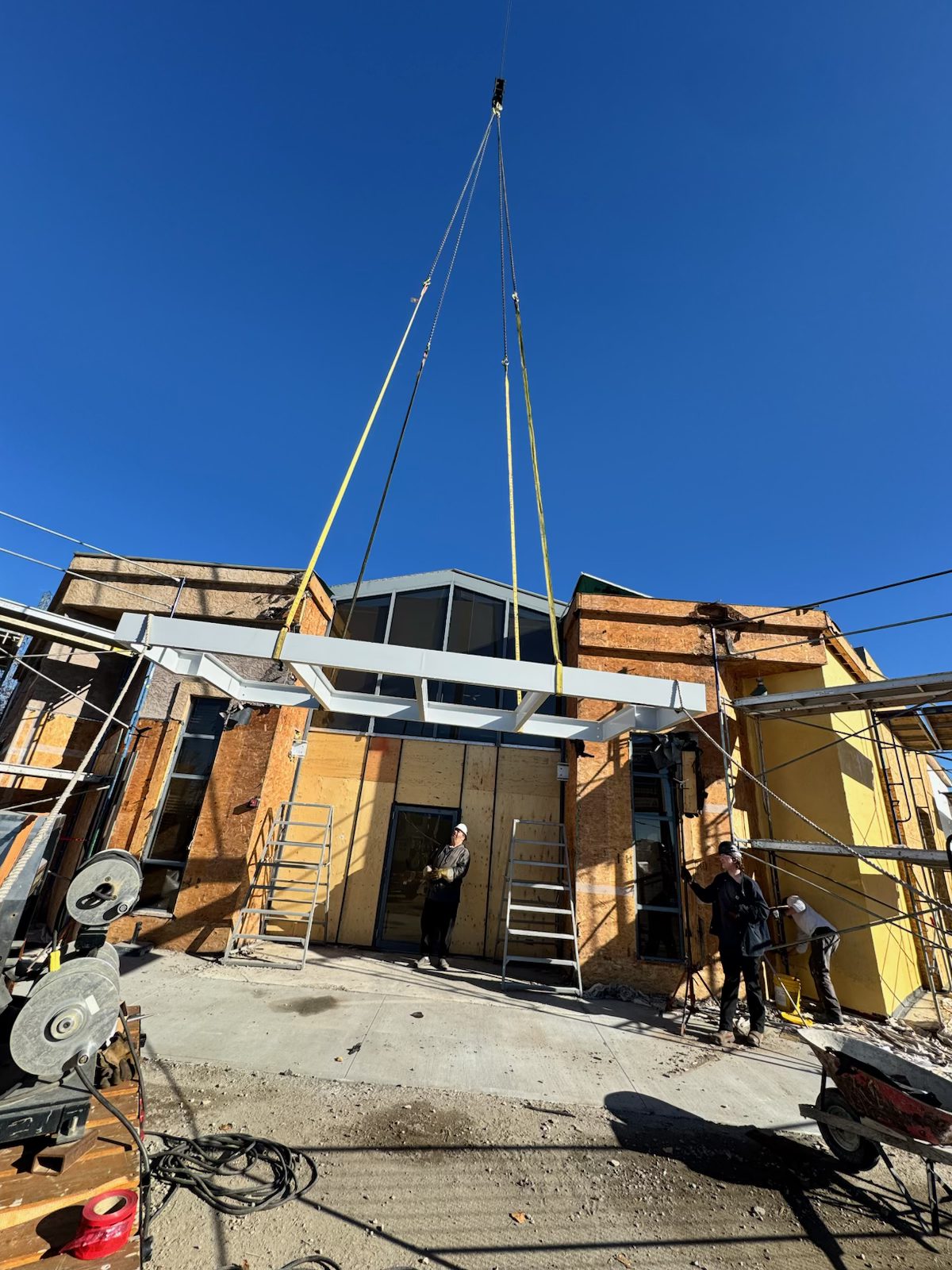 Crane lifts steel beam onto building under construction with workers — Blowers and Grafton (Red Deer)