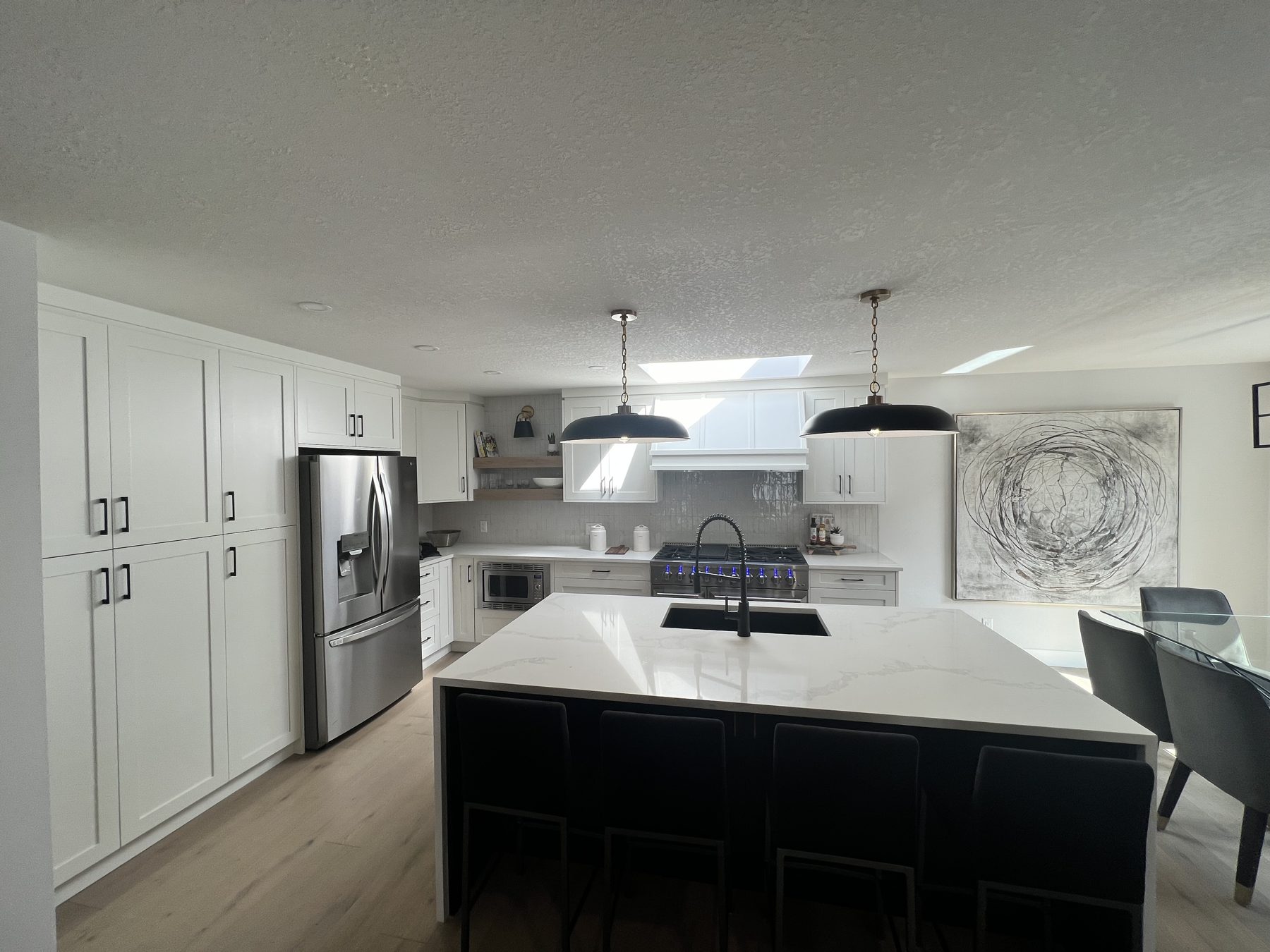 Modern kitchen renovation with white cabinets, island, and stainless steel appliances — 720 Lake Twintree Crescent SE, Calgary
