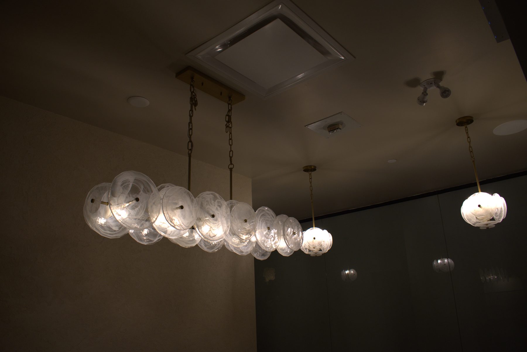 Modern glass chandeliers hanging from a textured wall ceiling — Leela Spa (Bankers Hall)