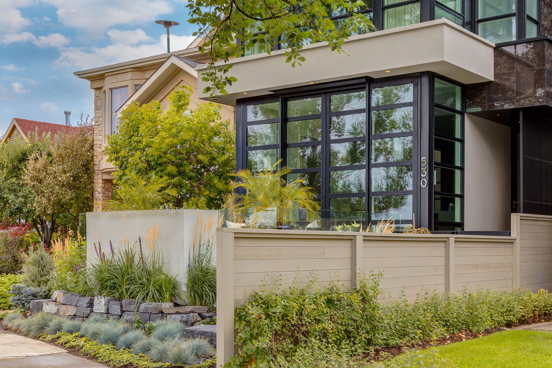 Modern house exterior with large glass doors, beige fence, and landscaping — Skyline