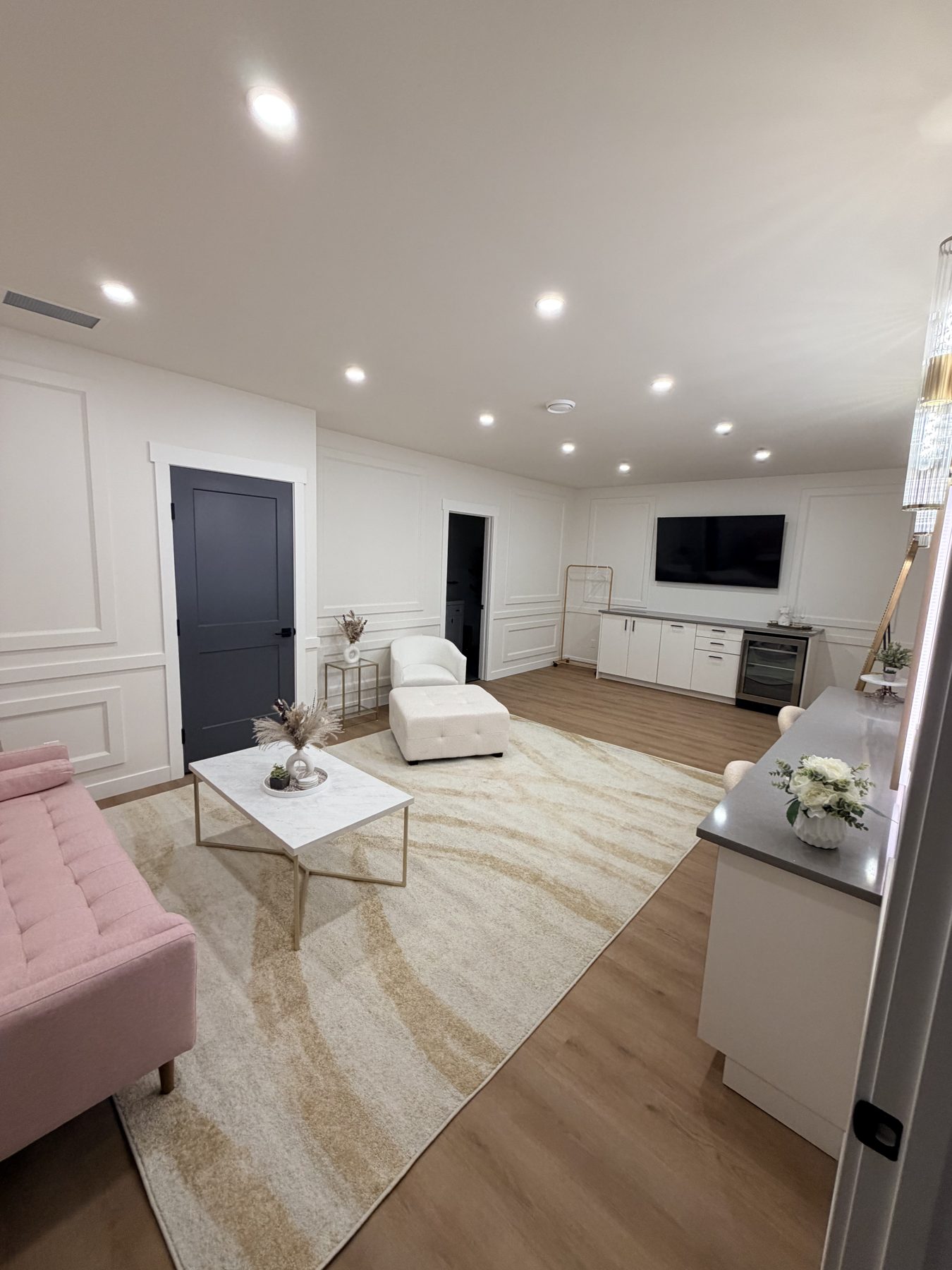 Renovated living room with white wainscoting, dark door, pink sofa, and wet bar — The Barron Venue