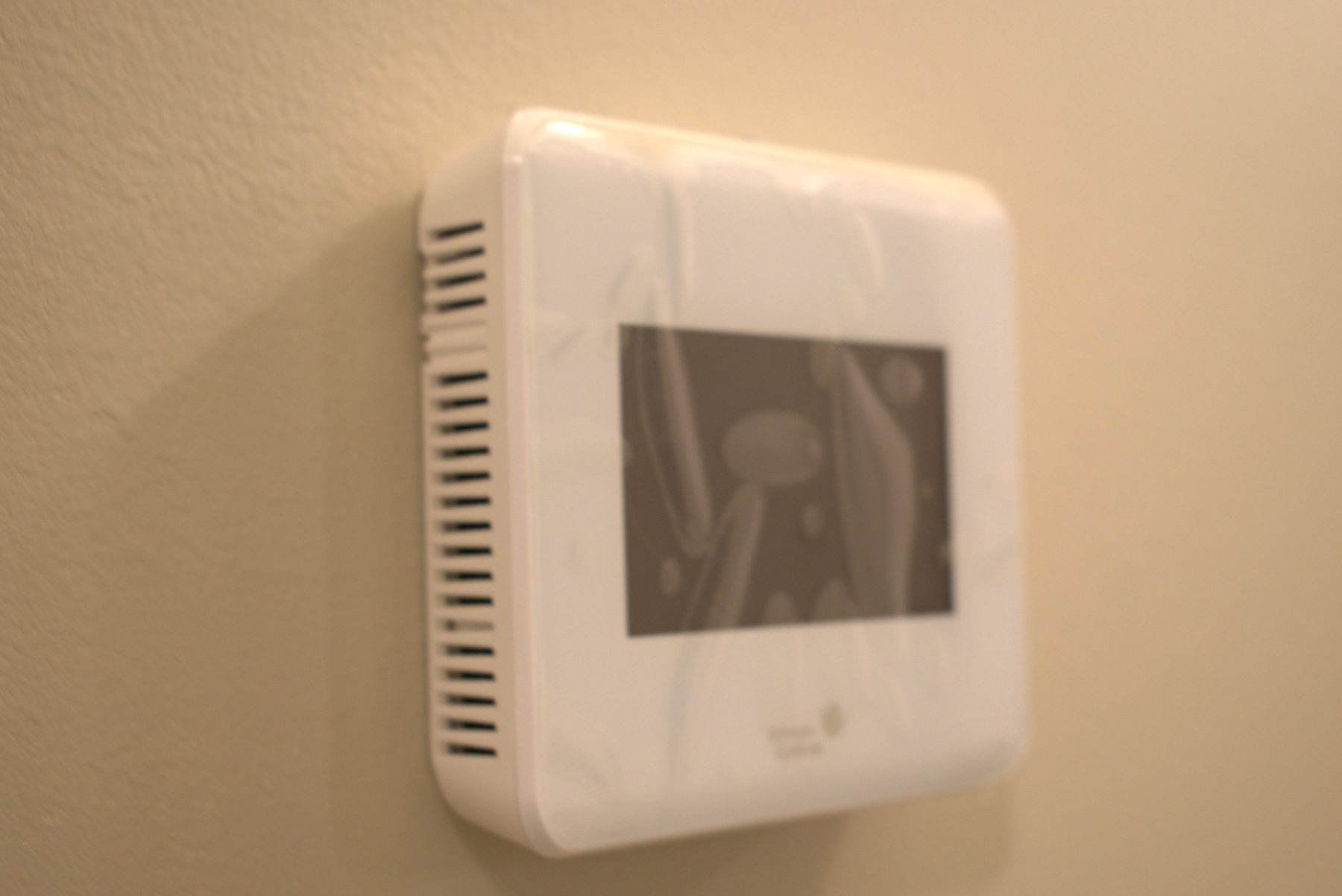 New white thermostat mounted on a tan wall, recently installed — Leela Spa (Bankers Hall)