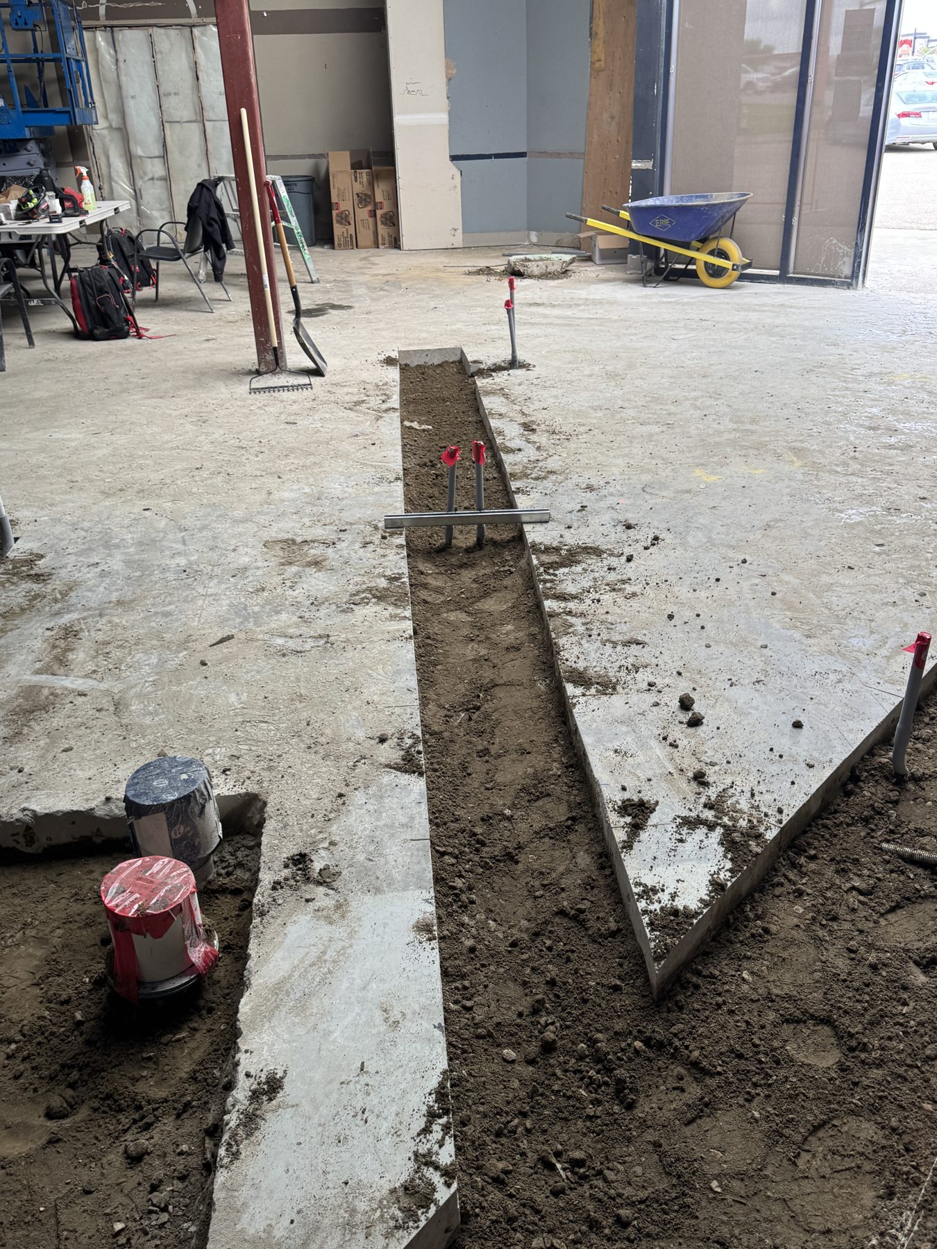 Concrete trench with piping, plumbing caps, and a wheelbarrow — Blowers and Grafton (Red Deer)
