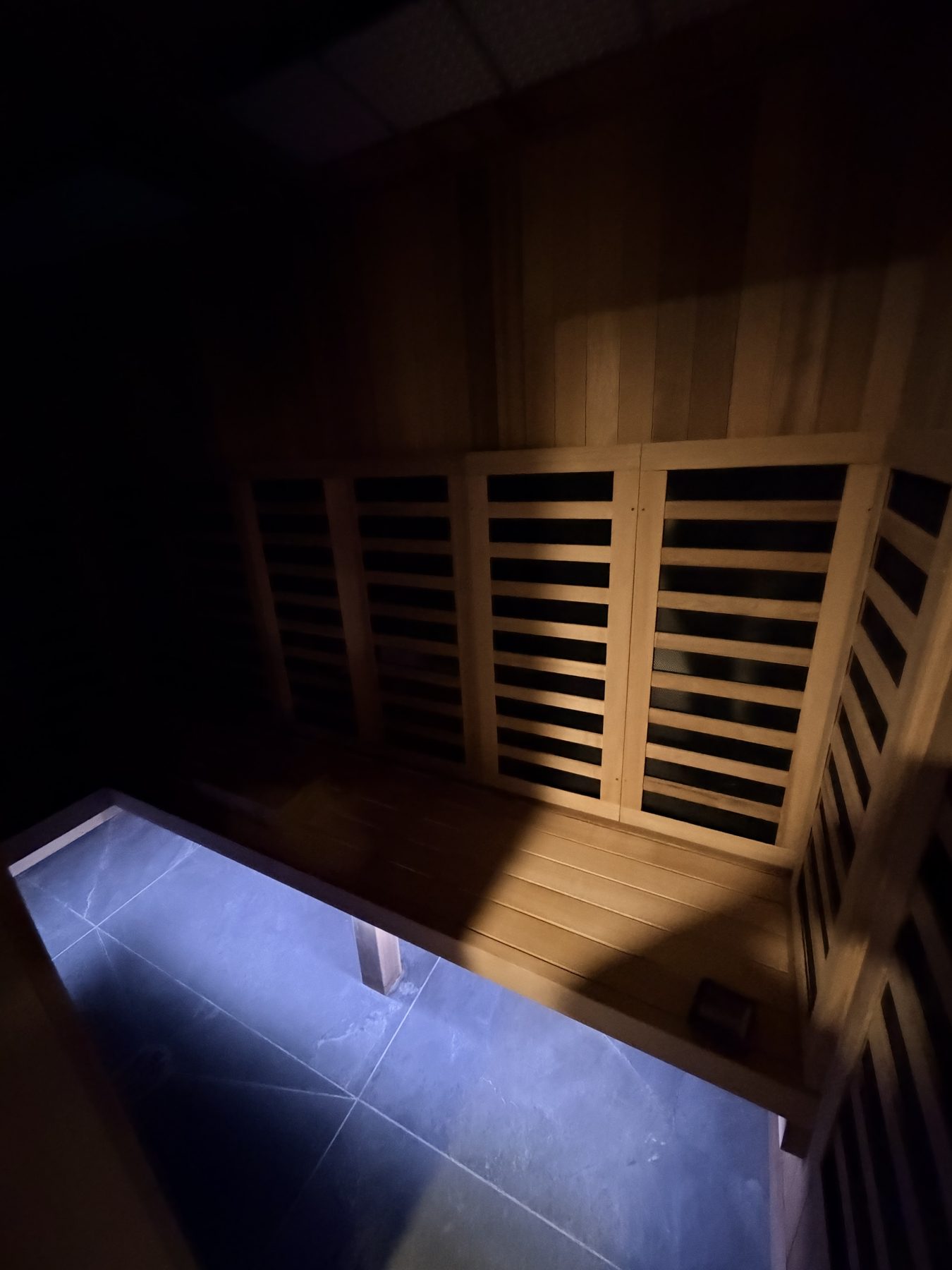 Wooden sauna benches and dark tiled floor in a partially lit room — Cedar Steam and Spa (Trinity Hills)