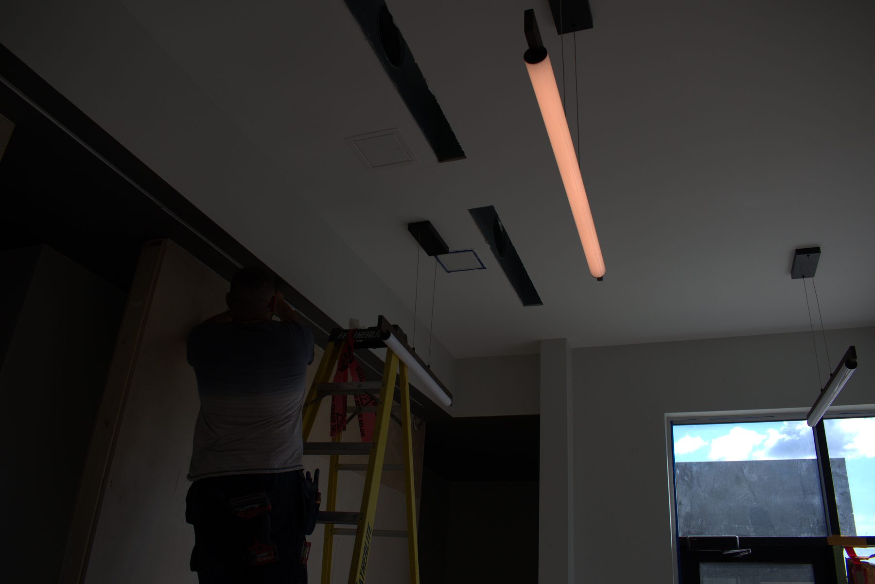 Worker installs contemporary pendant lights in unfinished modern ceiling — ONE8T (West District)
