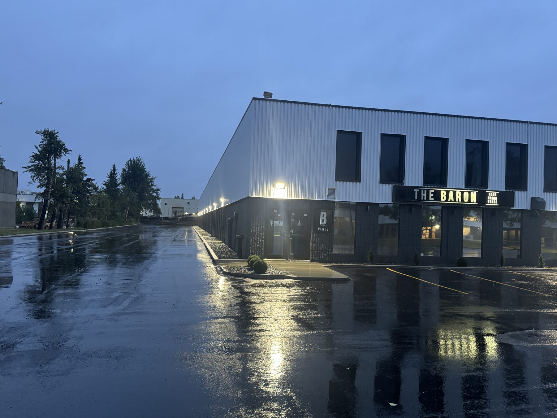 Wet asphalt reflects lights on modern building facade during evening — The Barron Venue by Onsite Contracting Services