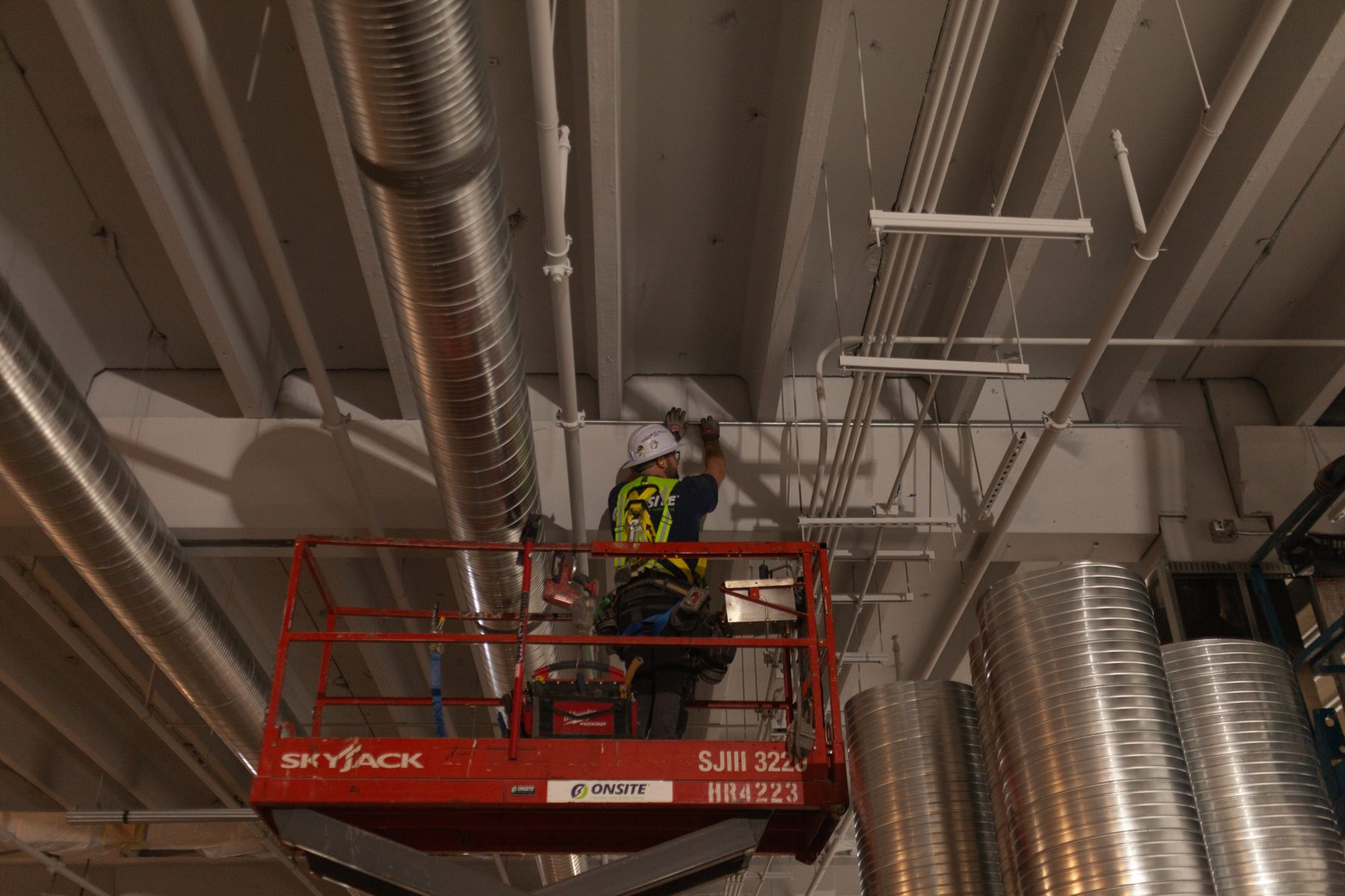 Worker on lift installing conduit near large metal ducts — Old Navy Chinook