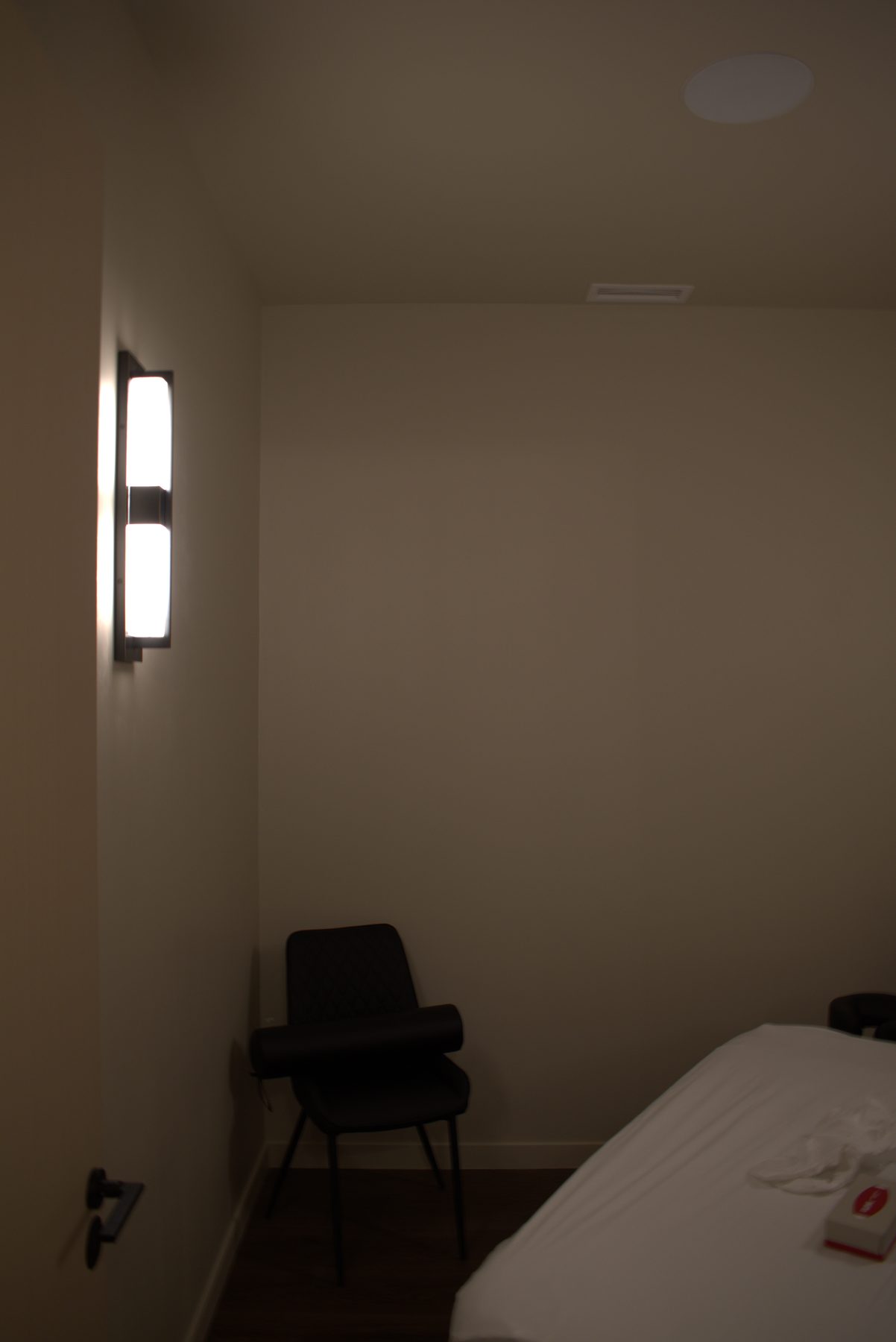 Spa room with massage table, chair, and wall sconce — Leela Spa (Bankers Hall)