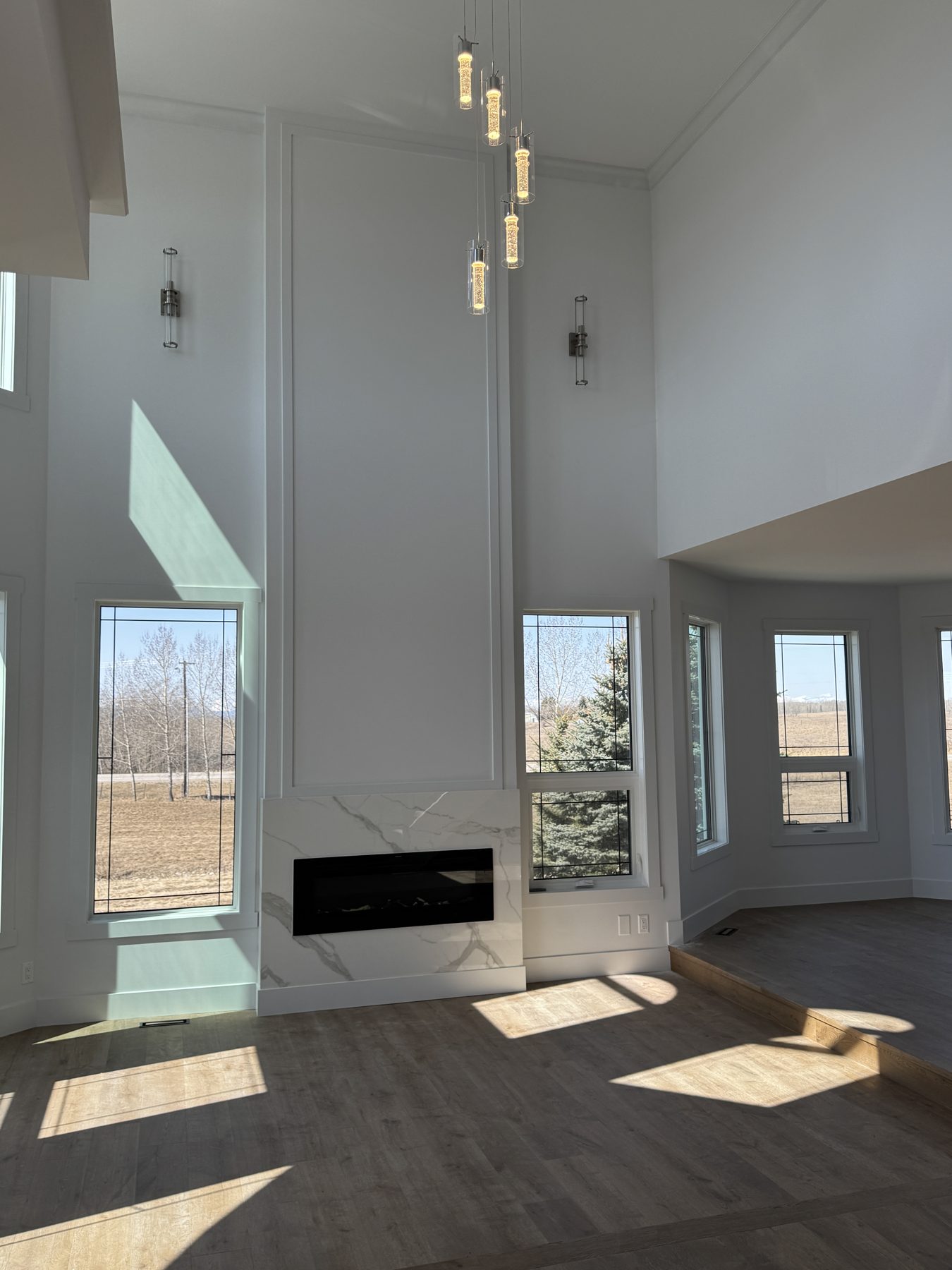 Modern living room with marble fireplace, wood floors, and pendant lights — 14 Lochend Drive, Cochrane