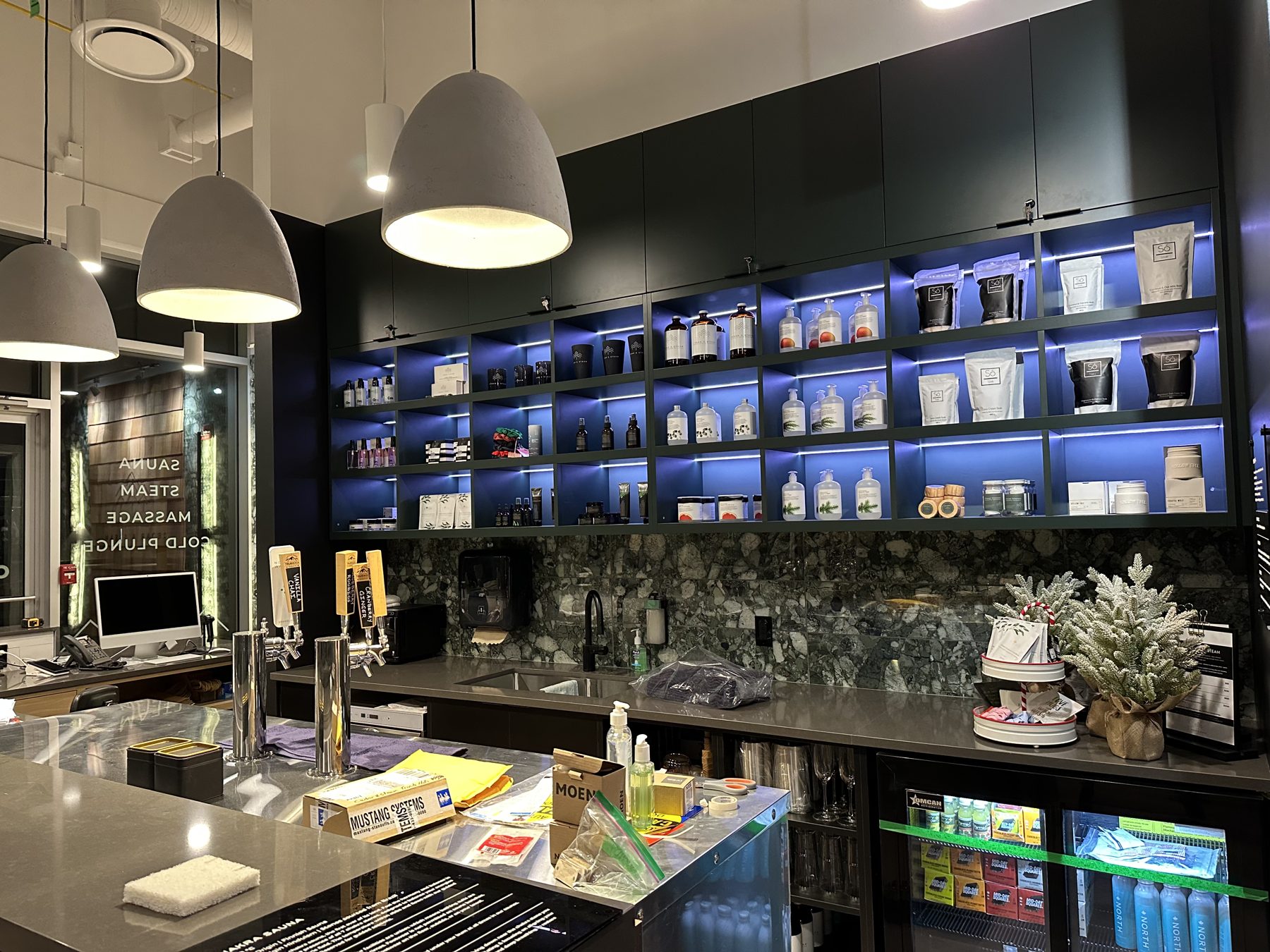 Shelves with product bottles and bags, bar with taps, and a mini fridge — Cedar Steam and Spa (Trinity Hills)