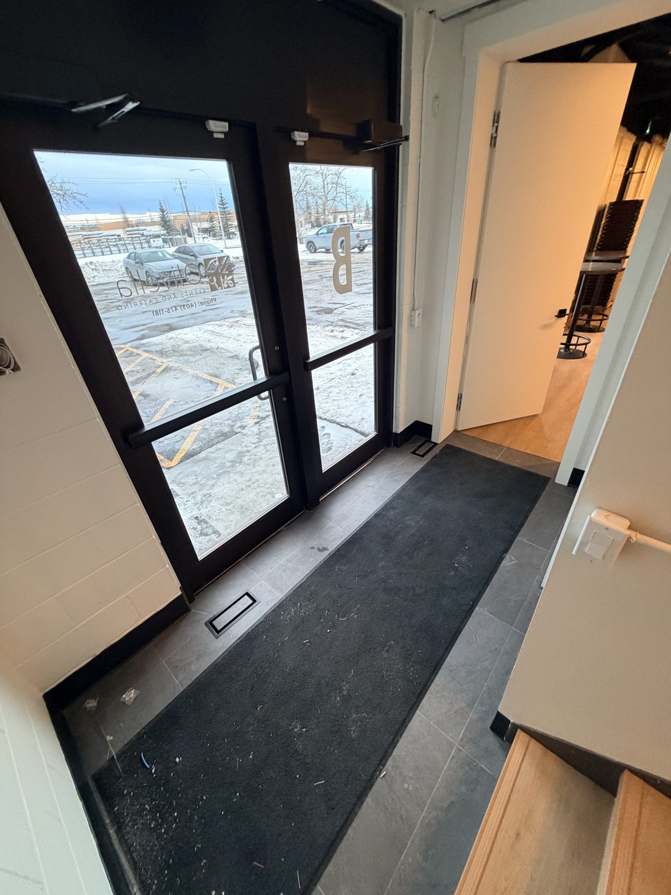 Entryway with double glass doors, dark frame, and black mat — The Barron Venue