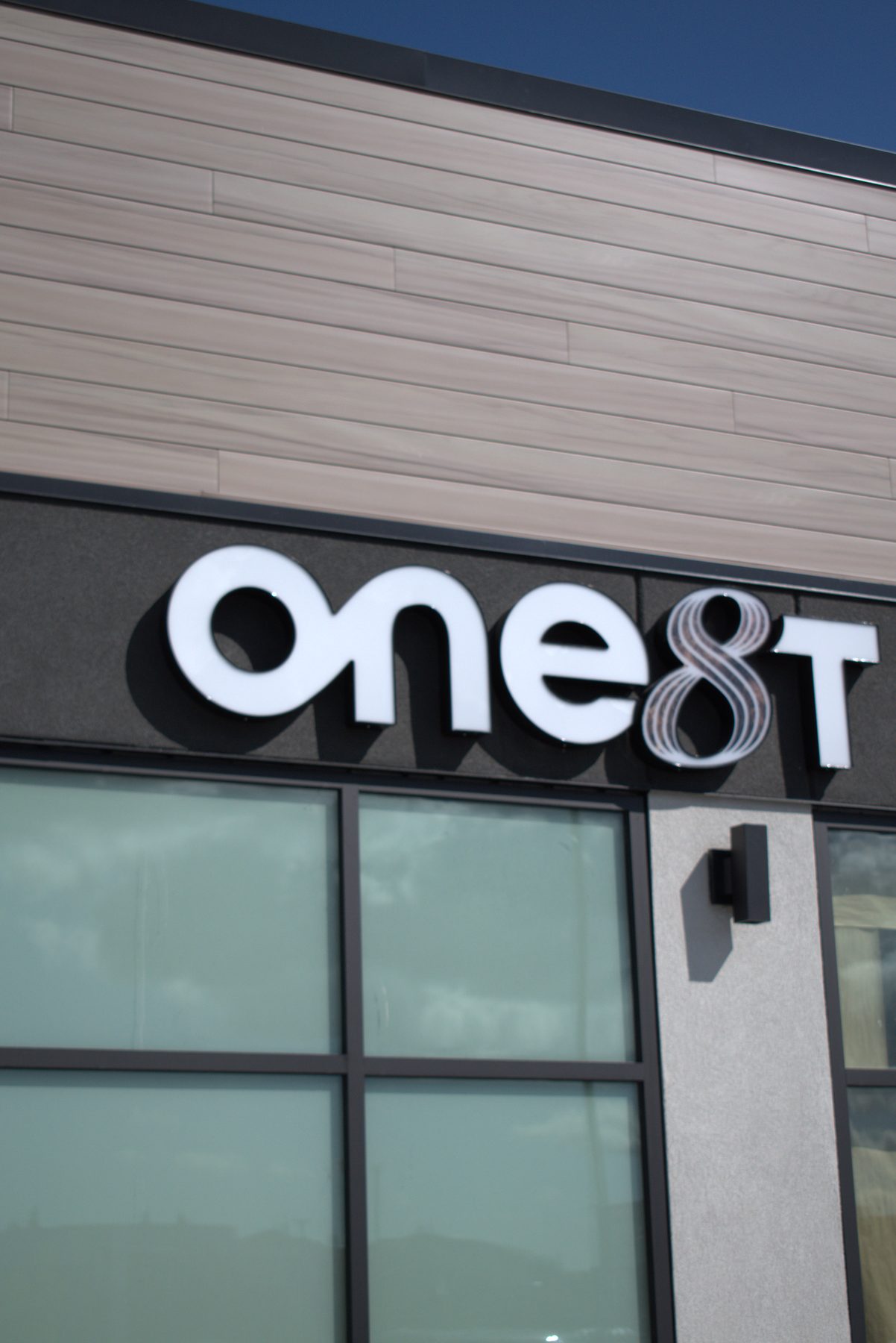 White illuminated sign on modern building facade with wood-look siding — ONE8T (West District)