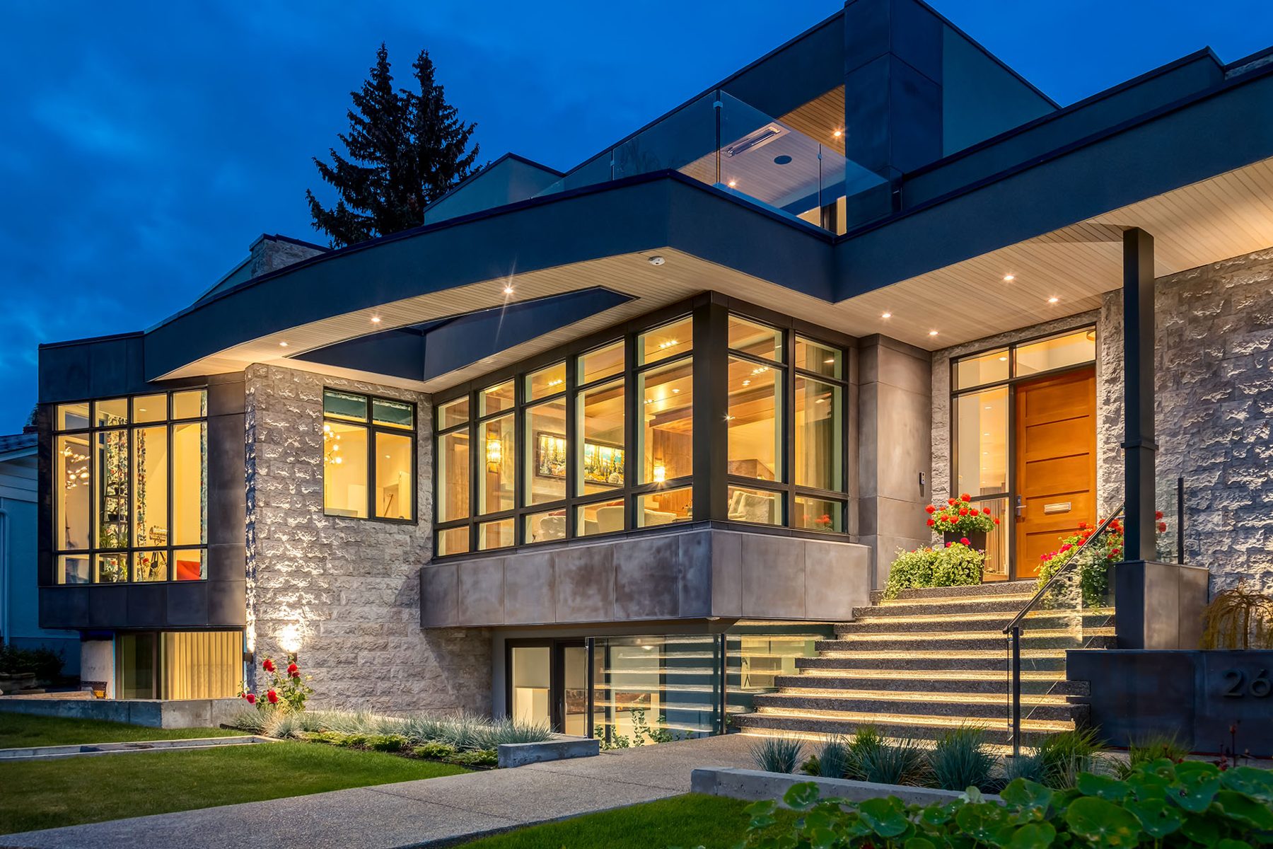 Modern home exterior with stone, wood, and glass elements illuminated at dusk — Evolution