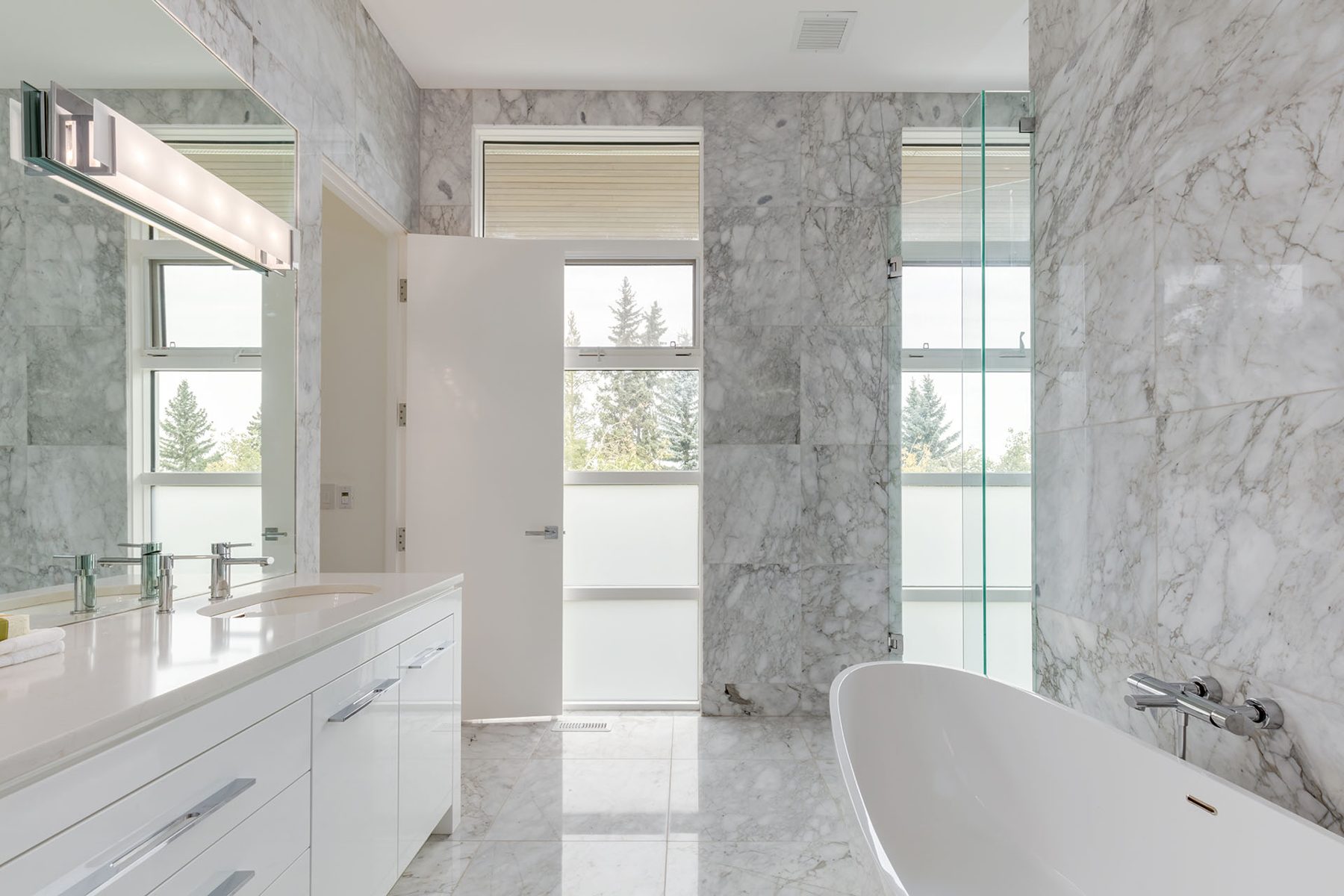 Marble bathroom with freestanding tub, vanity, and open door — Germania