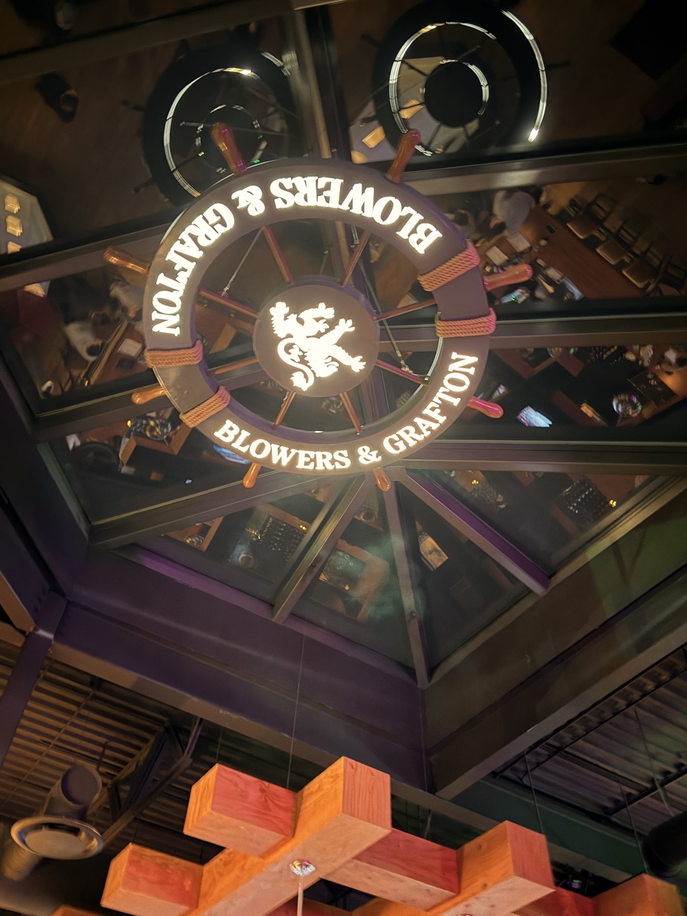 Ship's wheel sign above wooden beams, reflecting a bar interior — Blowers and Grafton (Red Deer)