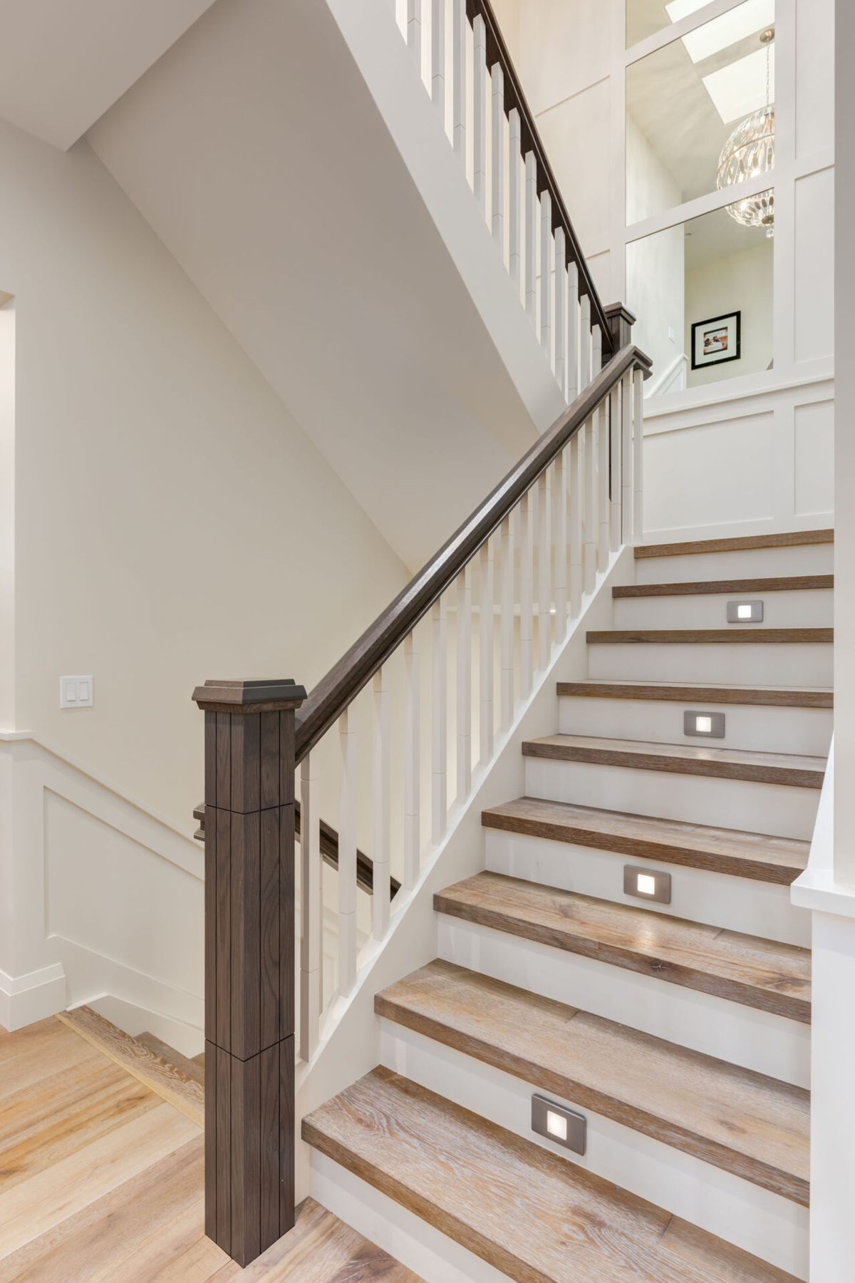 Staircase with white balusters, dark handrail, and wood treads with LED lights — Artista