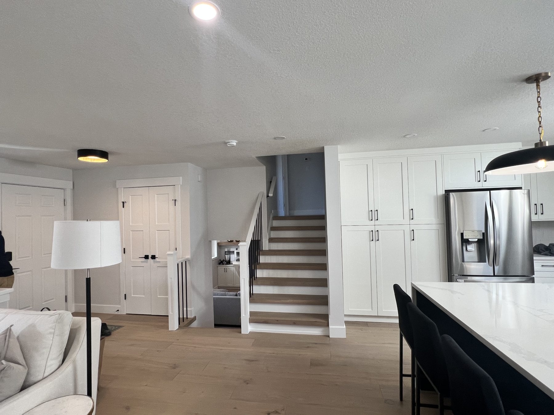 Modern kitchen renovation with white cabinets, stainless steel fridge, and staircase — 720 Lake Twintree Crescent SE, Calgary