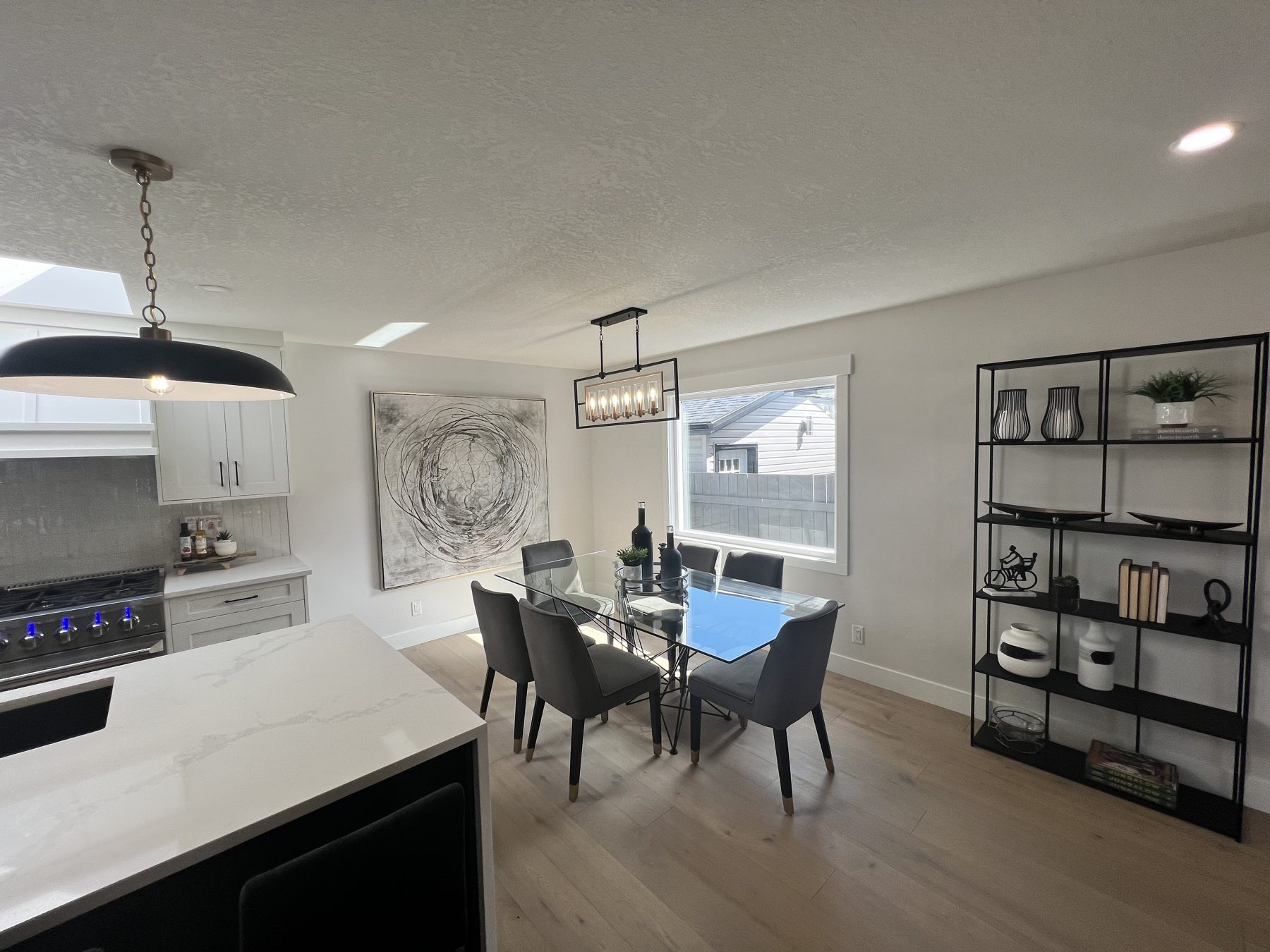 Dining area with glass table, chairs, modern shelving, and updated kitchen — 720 Lake Twintree Crescent SE, Calgary