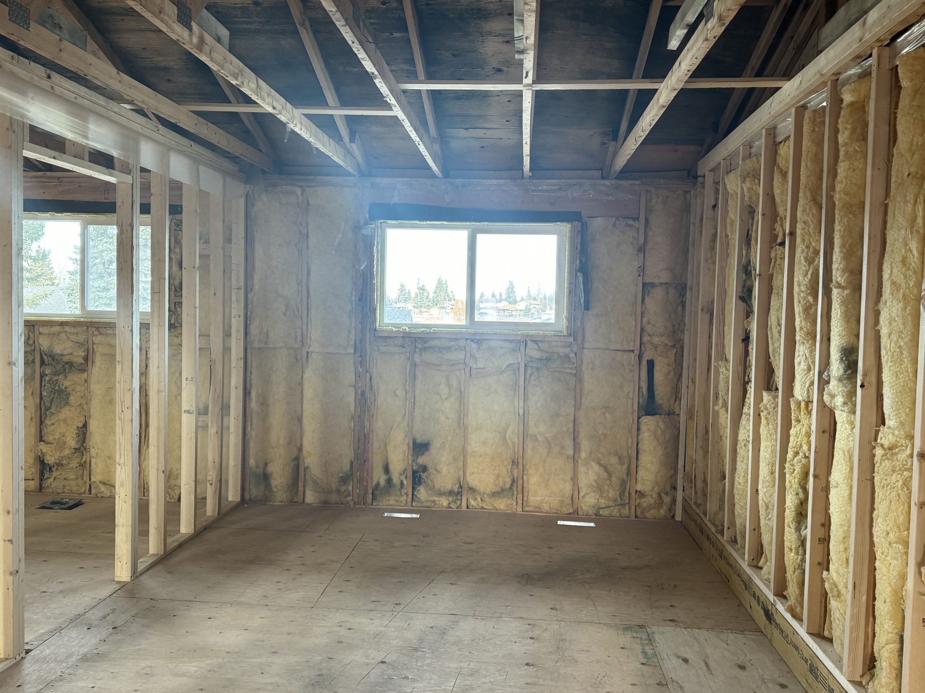 Framed room with exposed insulation, rough wooden floor, and ceiling joists — 188 Lake Adams Crescent SE, Calgary