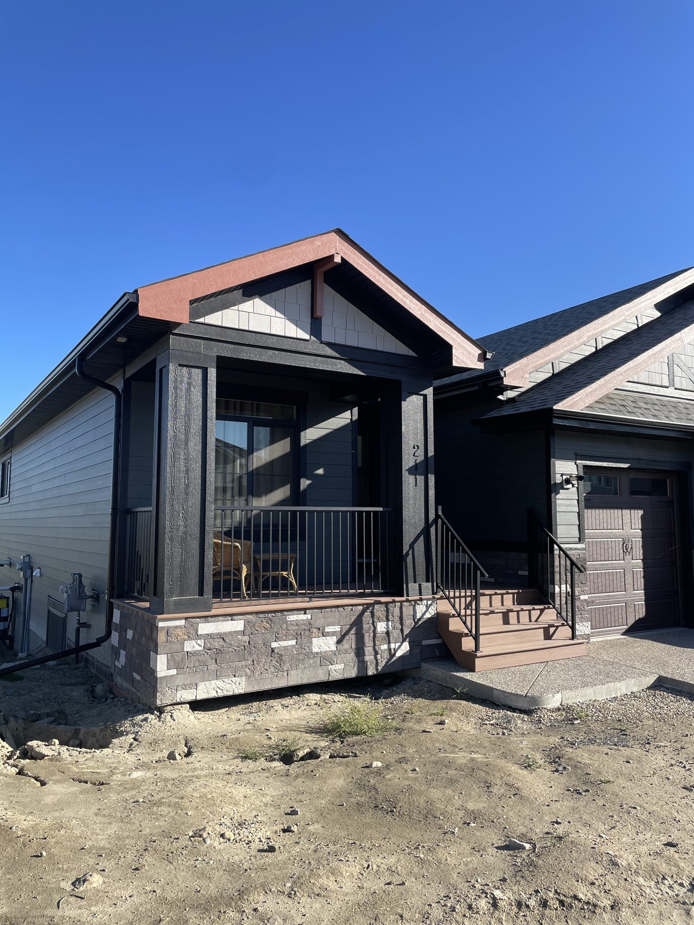New home exterior features dark siding, stone accent, and wood-look deck — 211 Blackstone Rd