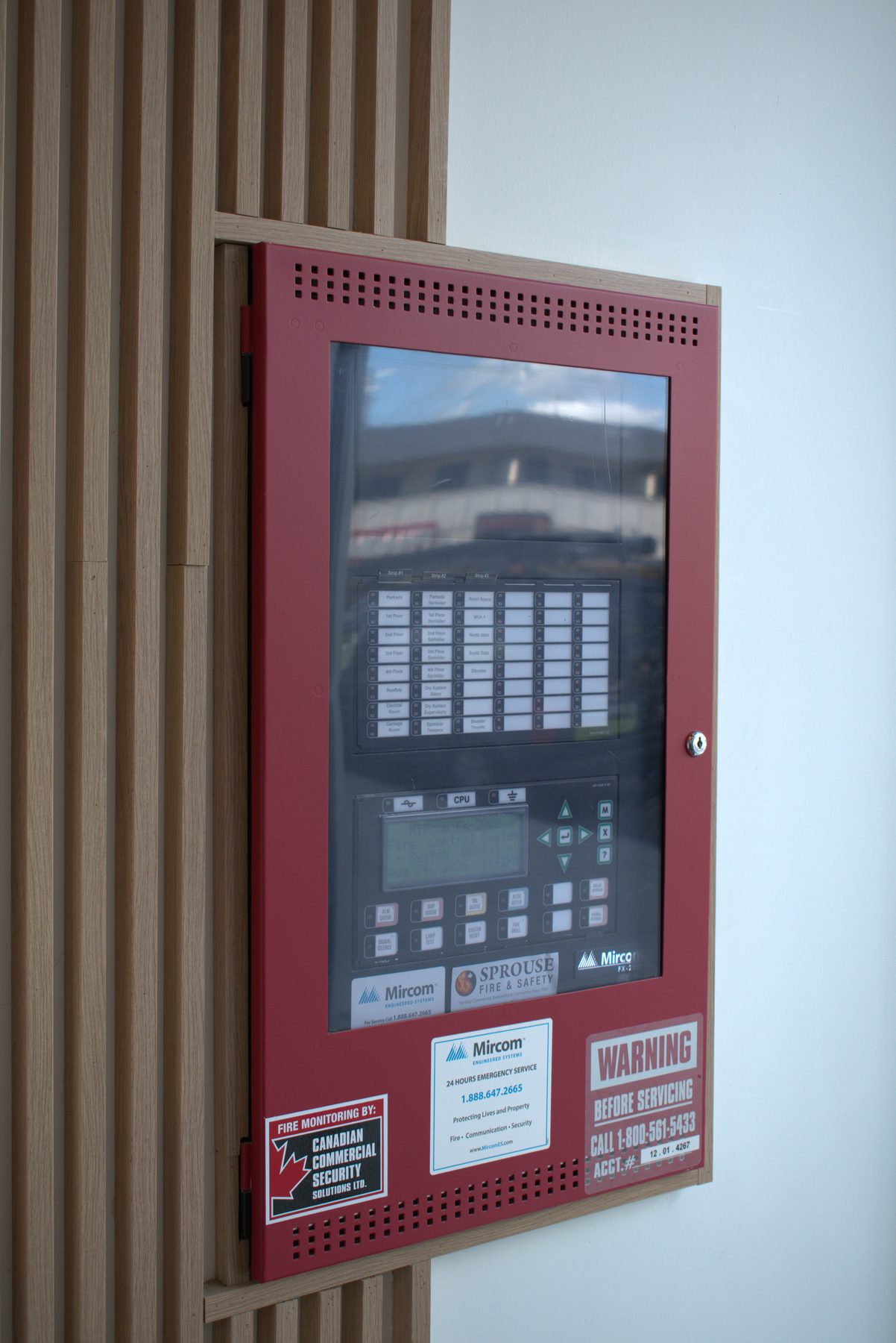 Red fire alarm panel installed on slatted wood accent wall — Big Buns (Bowness)