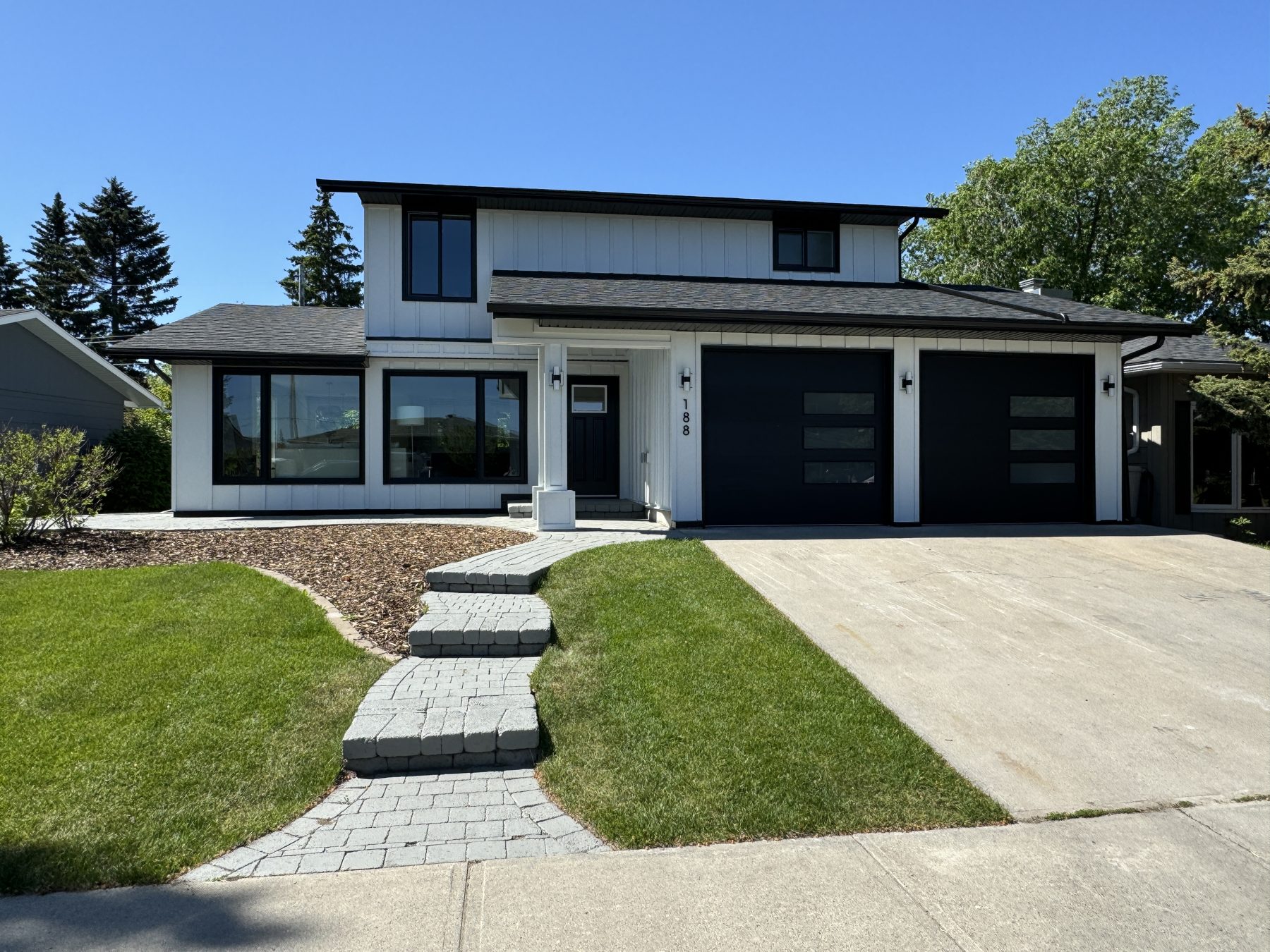 Modern white house with black trim, windows, garage doors, and pathway — 188 Lake Adams Crescent SE, Calgary