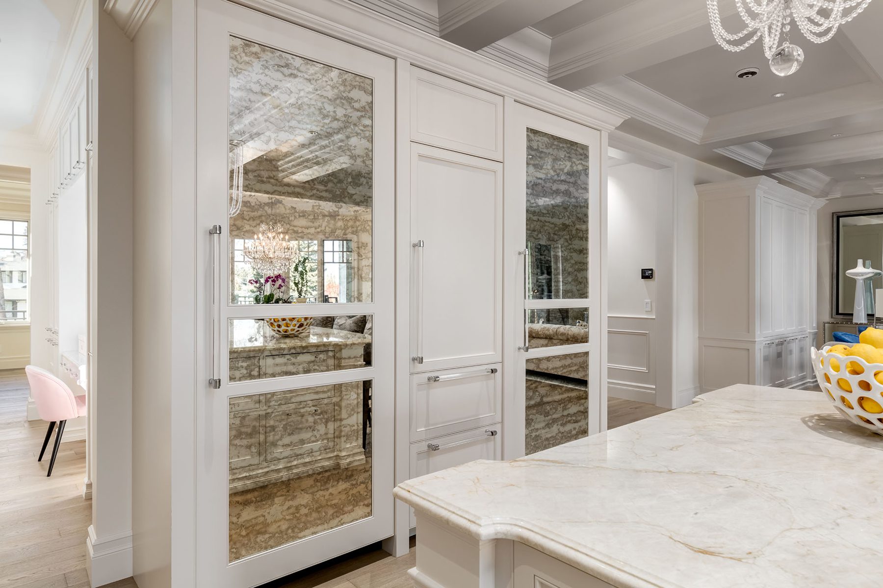 White kitchen cabinets with mirrored panels reflect a chandelier and island — White House