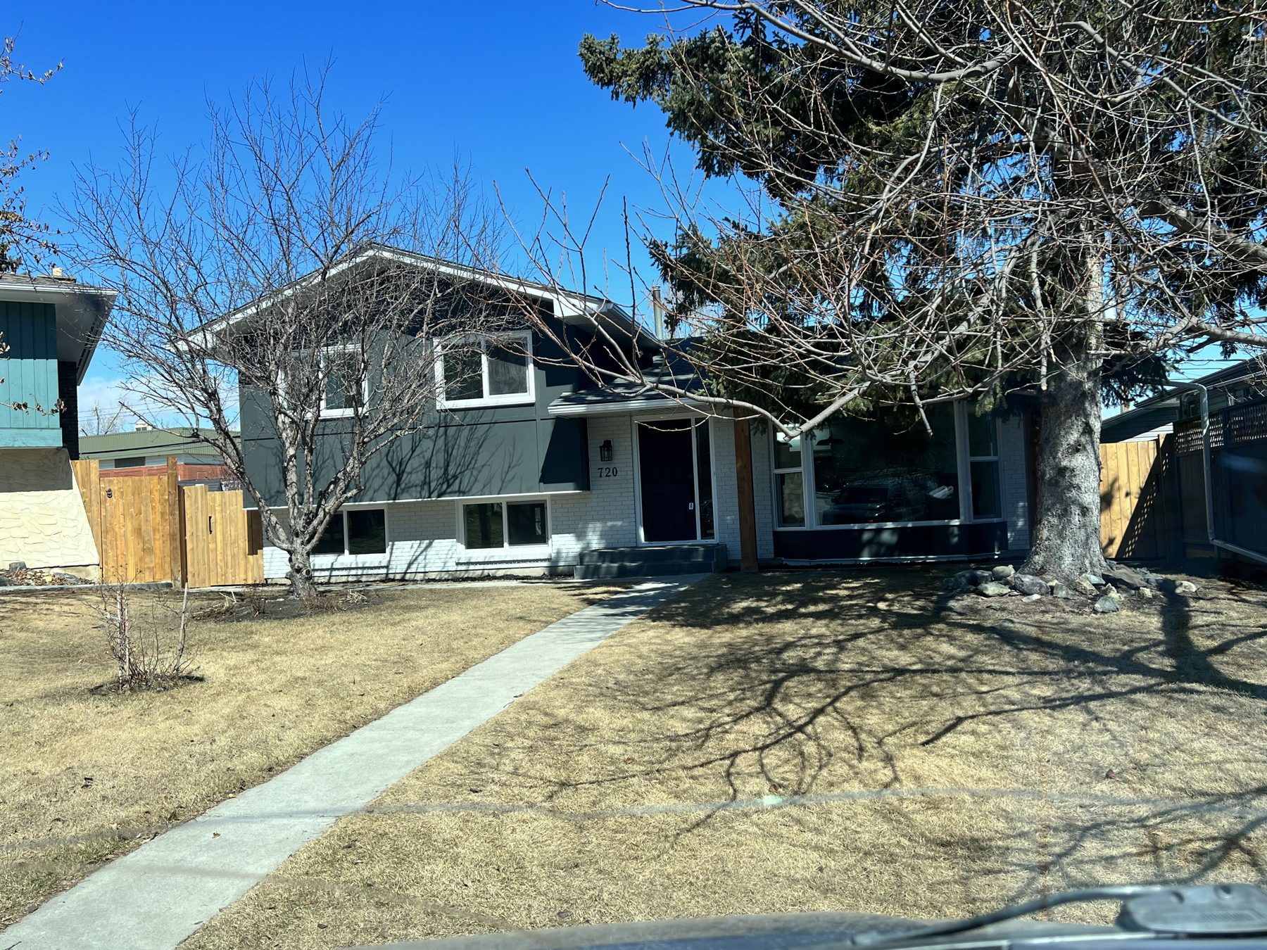 Modern house exterior with dark gray siding and white brick — 720 Lake Twintree Crescent SE, Calgary