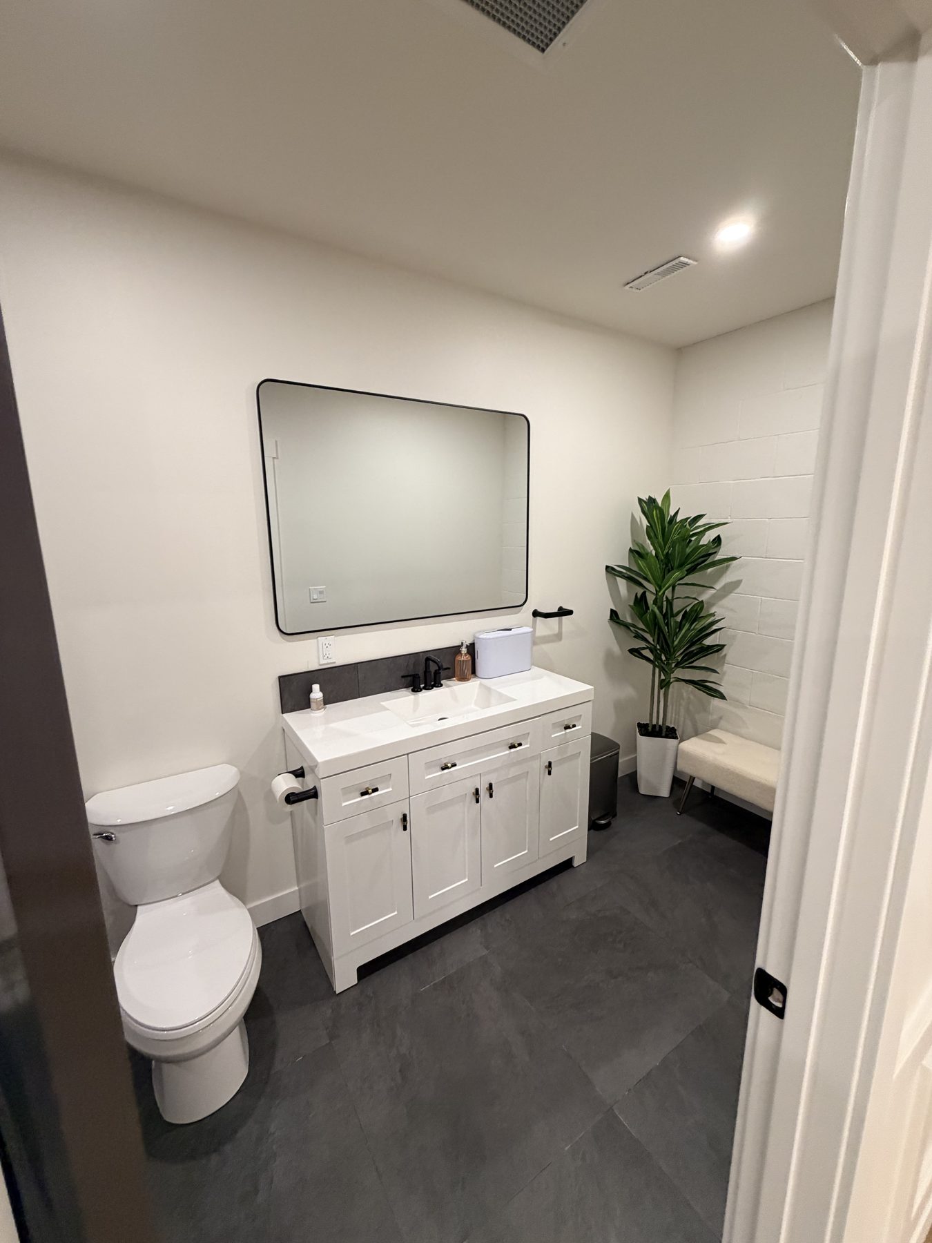 Modern bathroom with white vanity, black fixtures, and dark floor tiles — The Barron Venue
