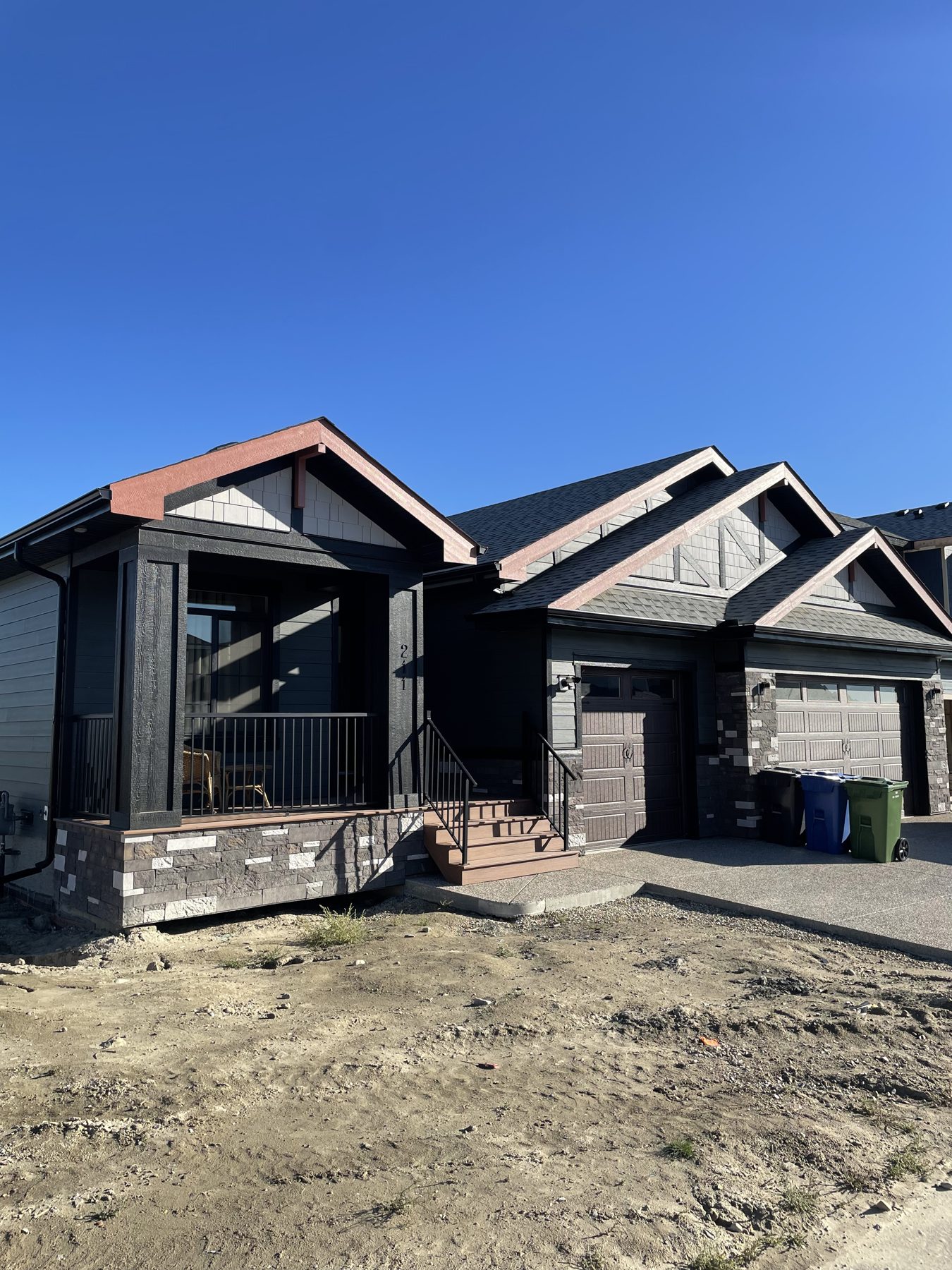 New home construction with dark siding, stone, and garages visible — 211 Blackstone Rd