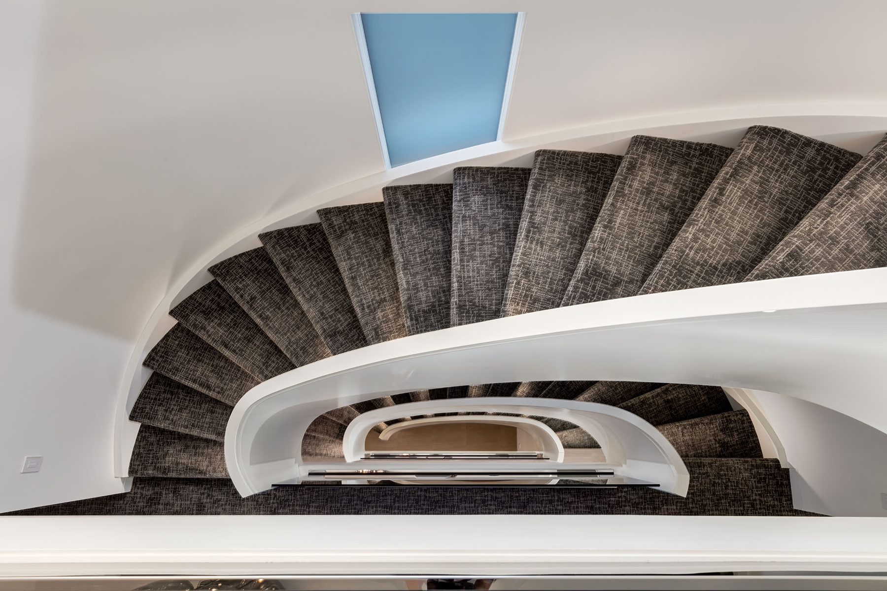 Curving modern staircase with dark patterned carpet and white railing — Skyline