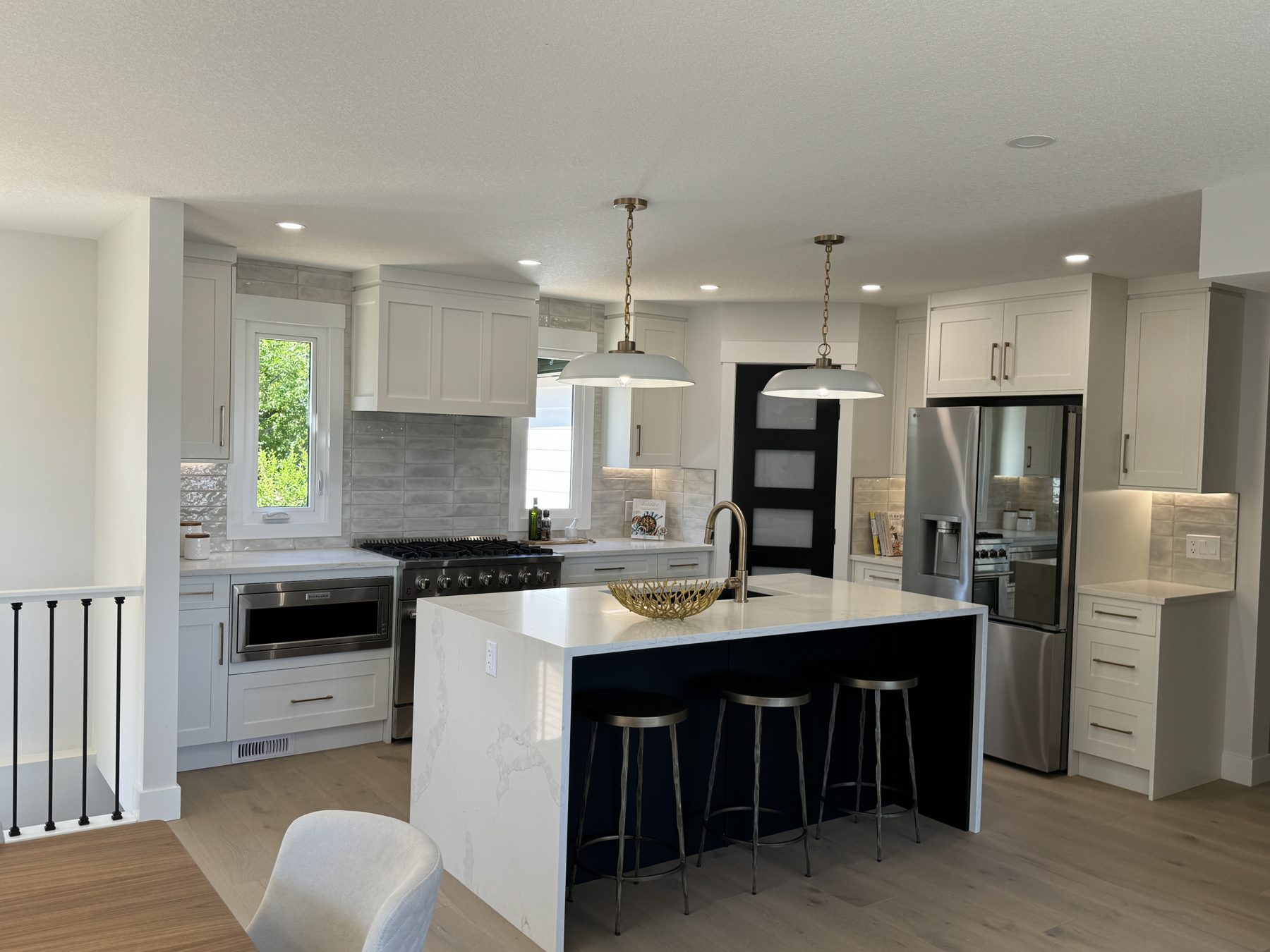 Modern kitchen renovation with white cabinets, island, stainless steel appliances, and pendant lights — Lake Bonavista