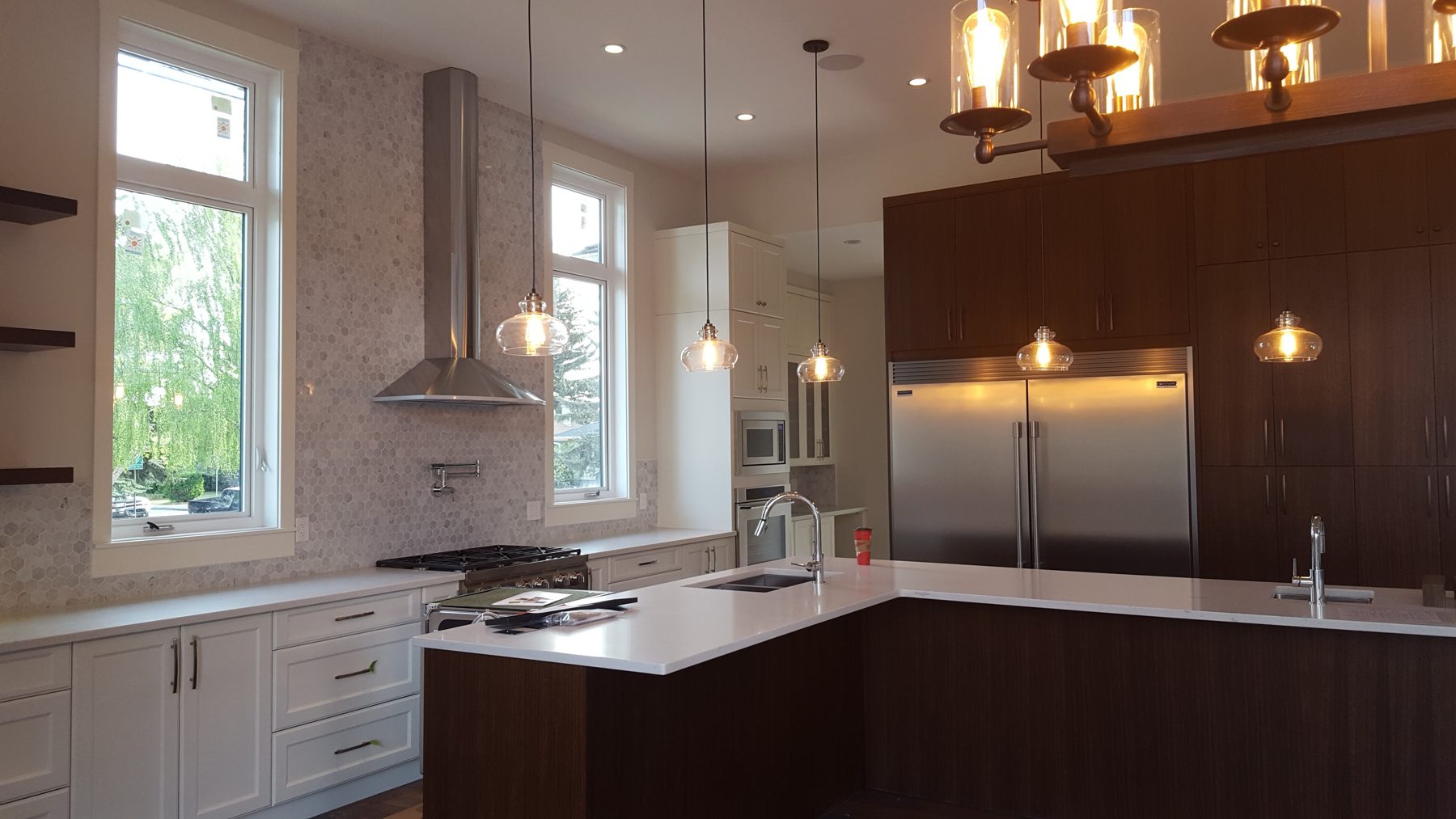 Modern kitchen with white cabinets, dark island, stainless steel appliances, and pendant lights — Briar Hill