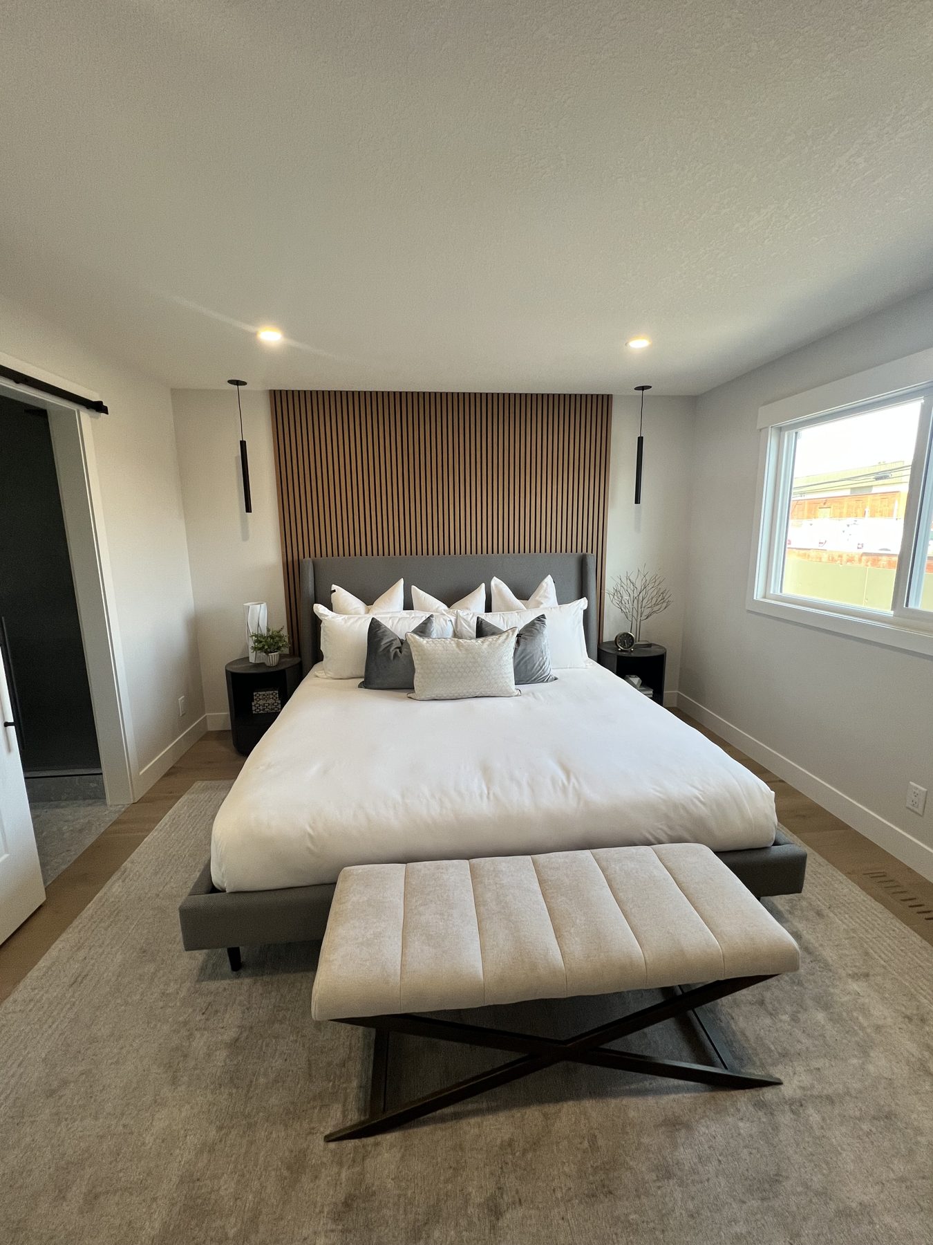 Modern bedroom with wood slat headboard and upholstered bench — 720 Lake Twintree Crescent SE, Calgary