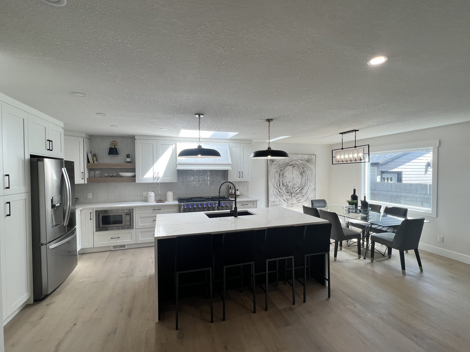 Modern kitchen with white cabinets, black island, and dining area — 720 Lake Twintree Crescent SE, Calgary by Onsite Contracting Services