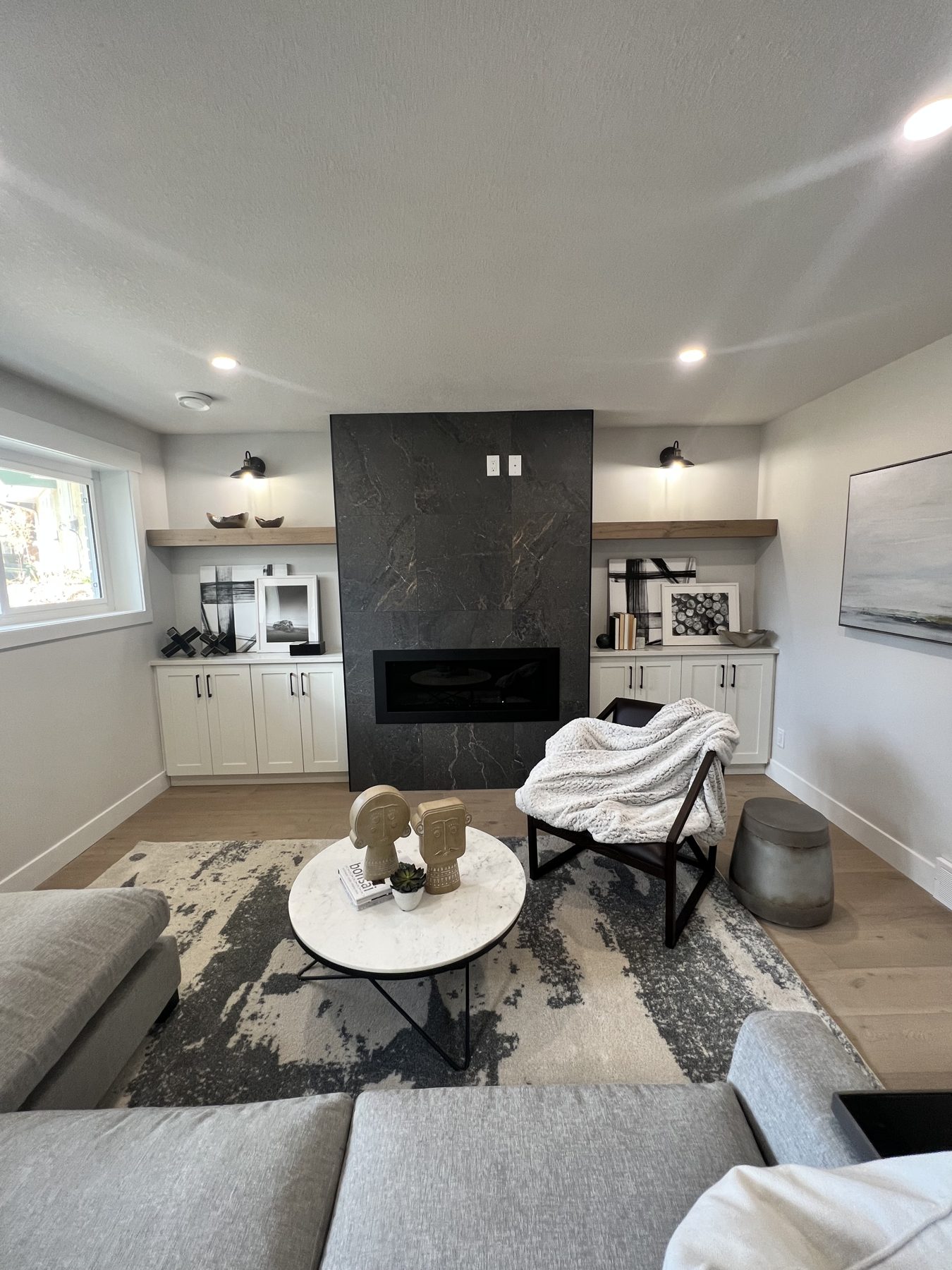 Modern living room with charcoal fireplace, white cabinets, and wood shelves — 720 Lake Twintree Crescent SE, Calgary