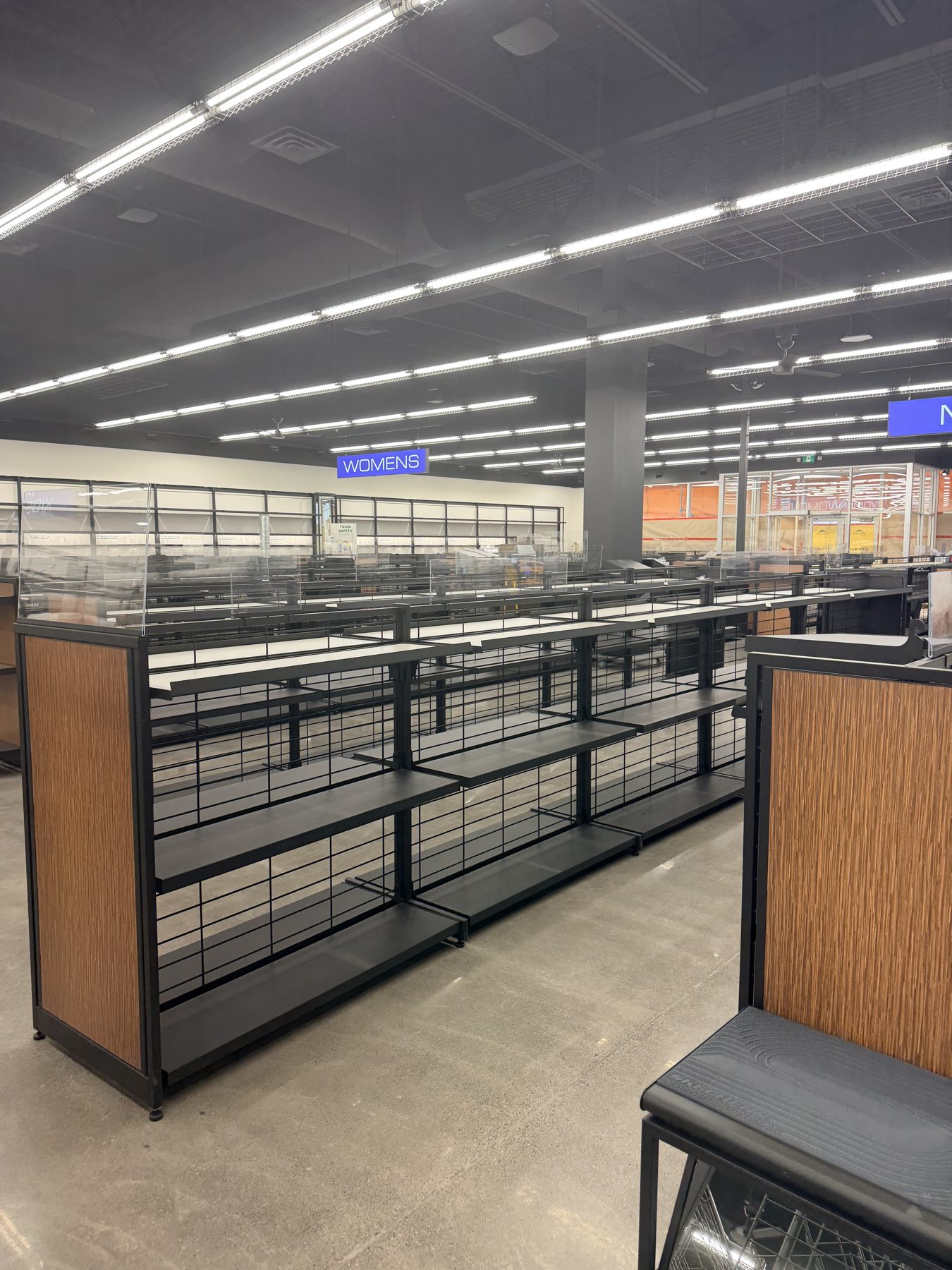 Empty retail store shelves and displays with "WOMENS" sign above — Skechers (Signal Hill)