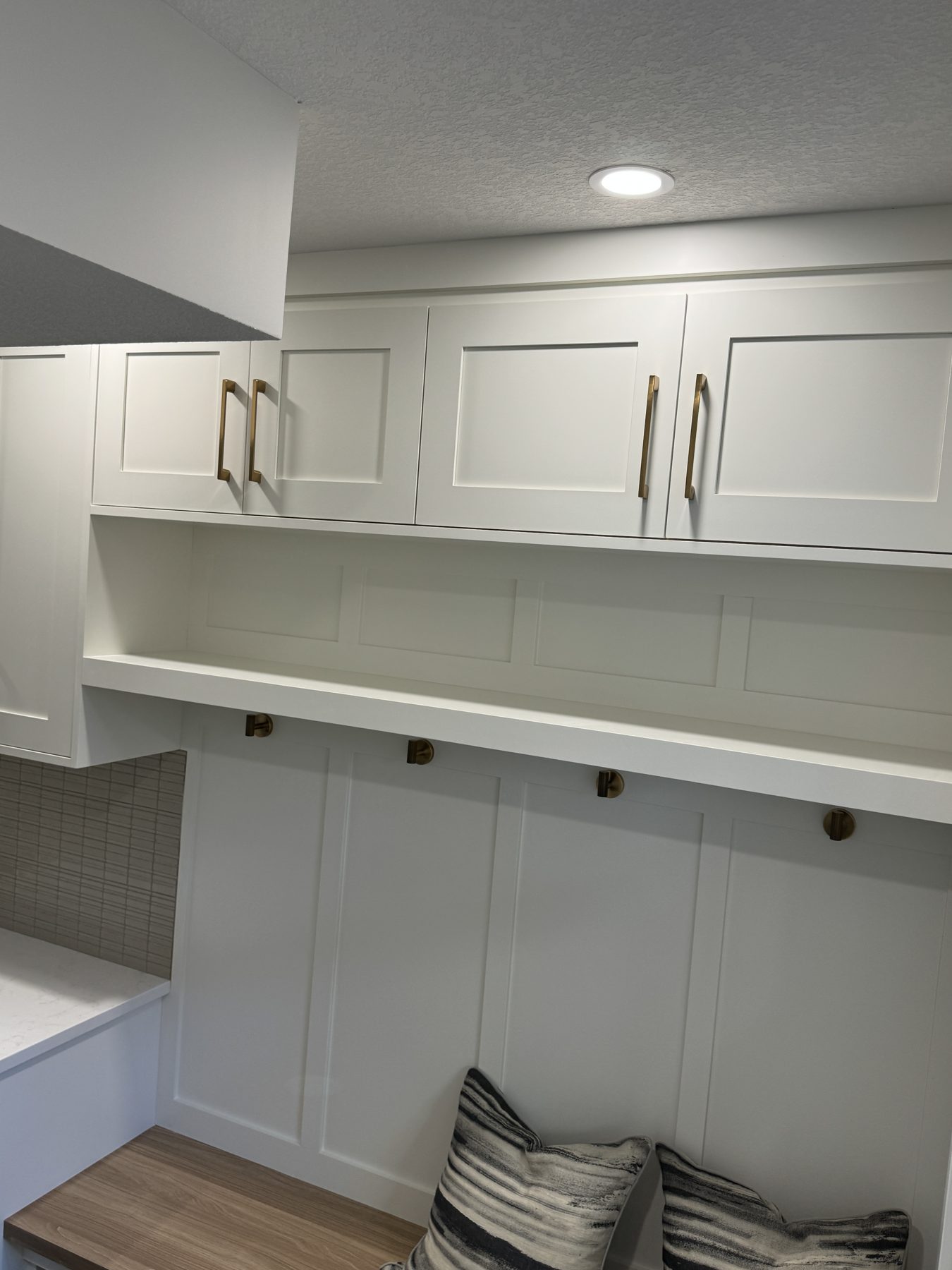 White mudroom built-ins with wood bench and brass hardware — Lake Bonavista