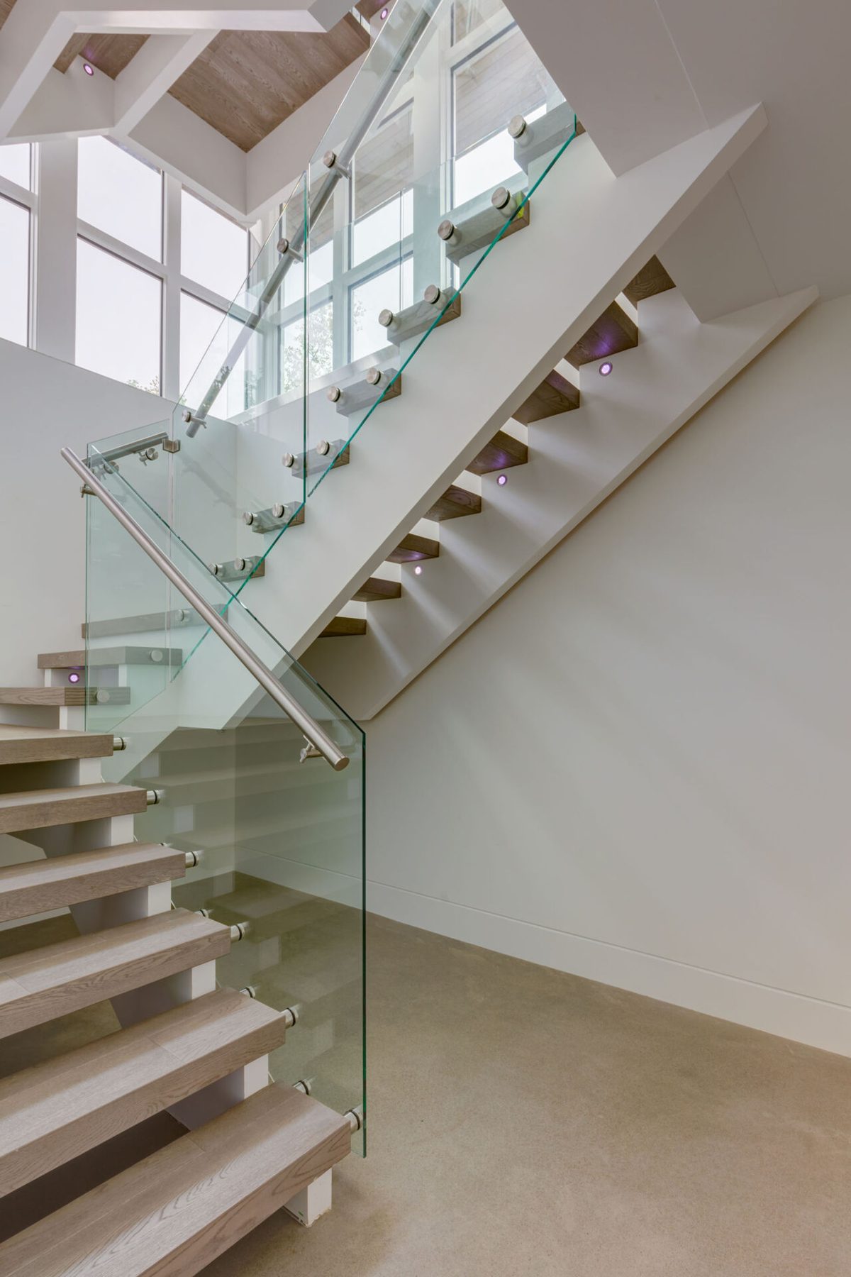 Modern floating wood staircase with glass railing and subtle step lighting — Germania