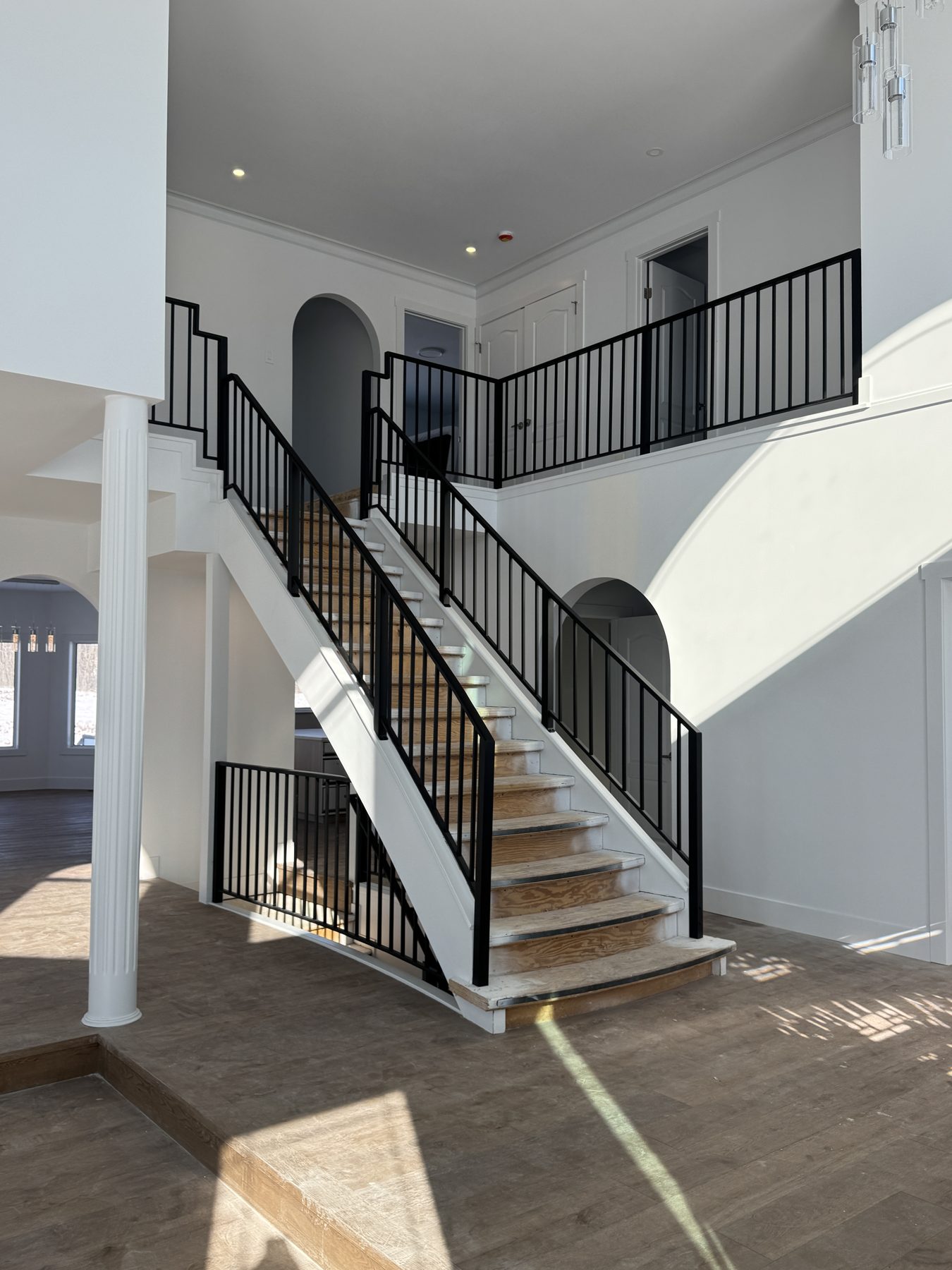 Unfinished staircase with black railings and wood treads, contemporary hall — 14 Lochend Drive, Cochrane