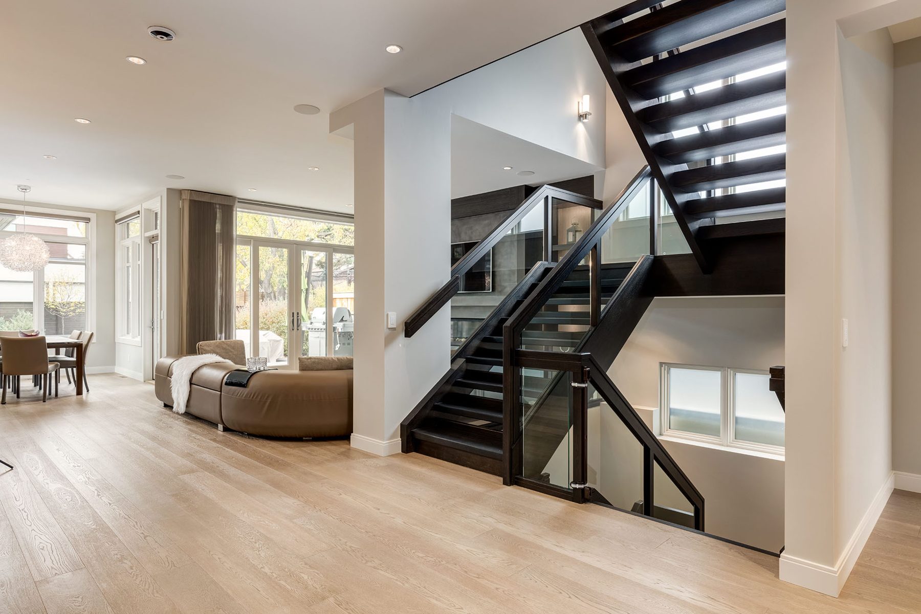 Modern dark wood staircase with glass railing, light wood floors, and furniture — The Cellar