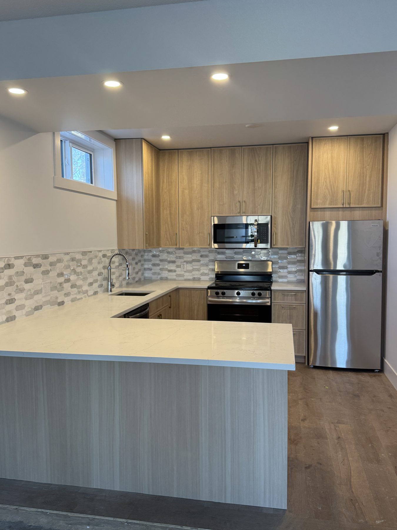 Modern kitchen renovation with light wood cabinets, quartz counters, stainless appliances — 14 Lochend Drive, Cochrane