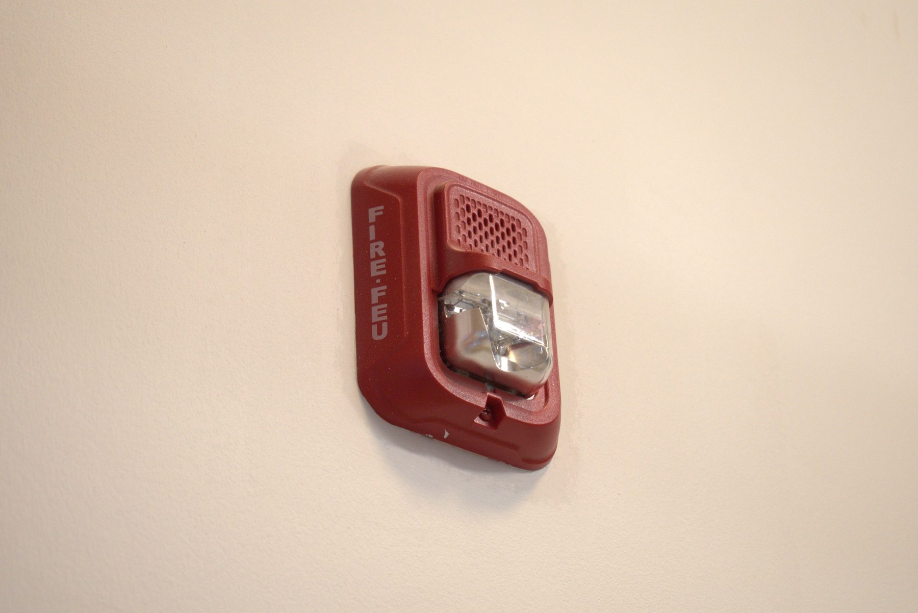 Red fire alarm with strobe light mounted on a cream wall — Big Buns (Bowness)