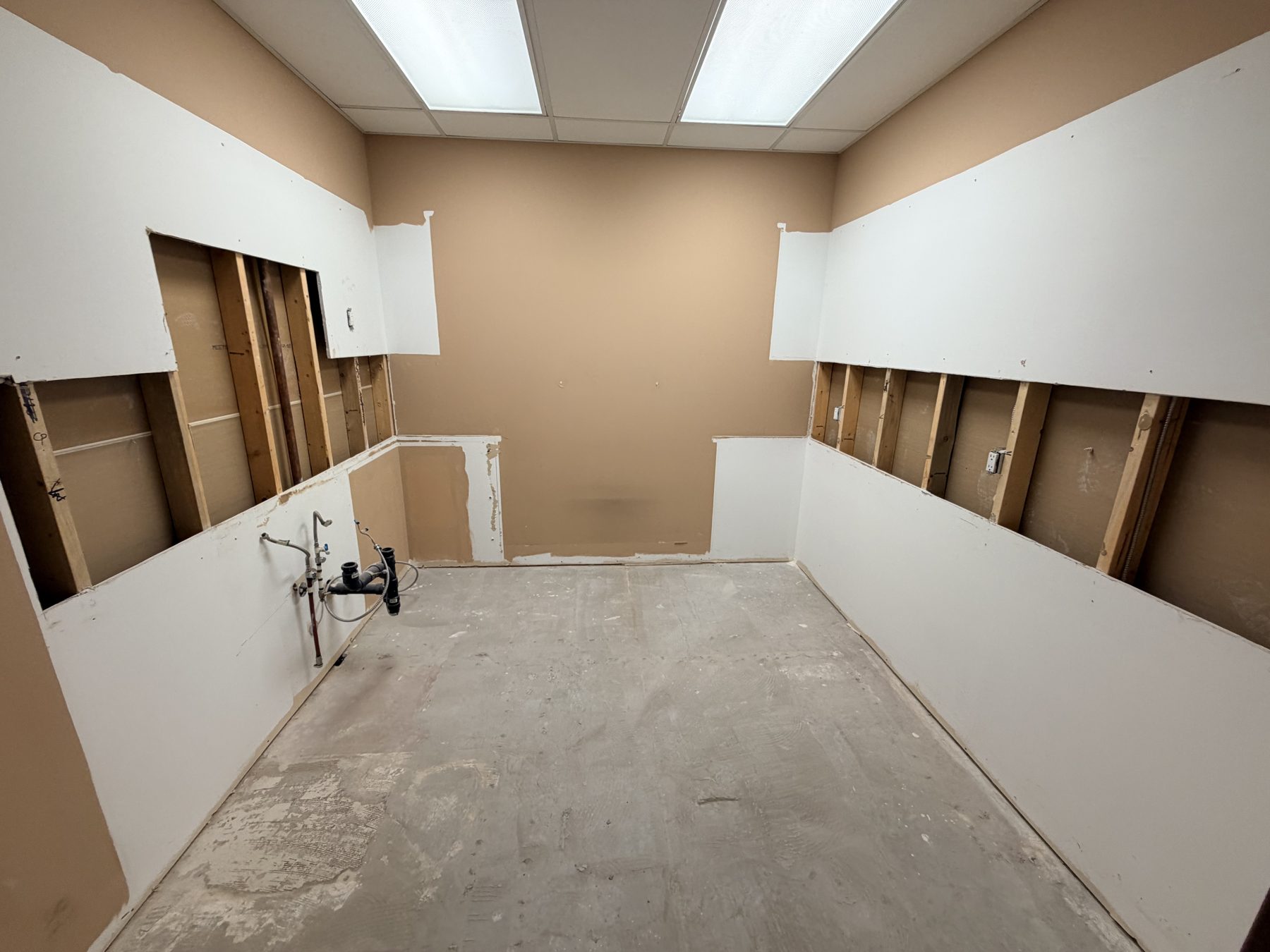 Kitchen renovation, drywall partially installed, plumbing visible, bare concrete floor — The Barron Venue