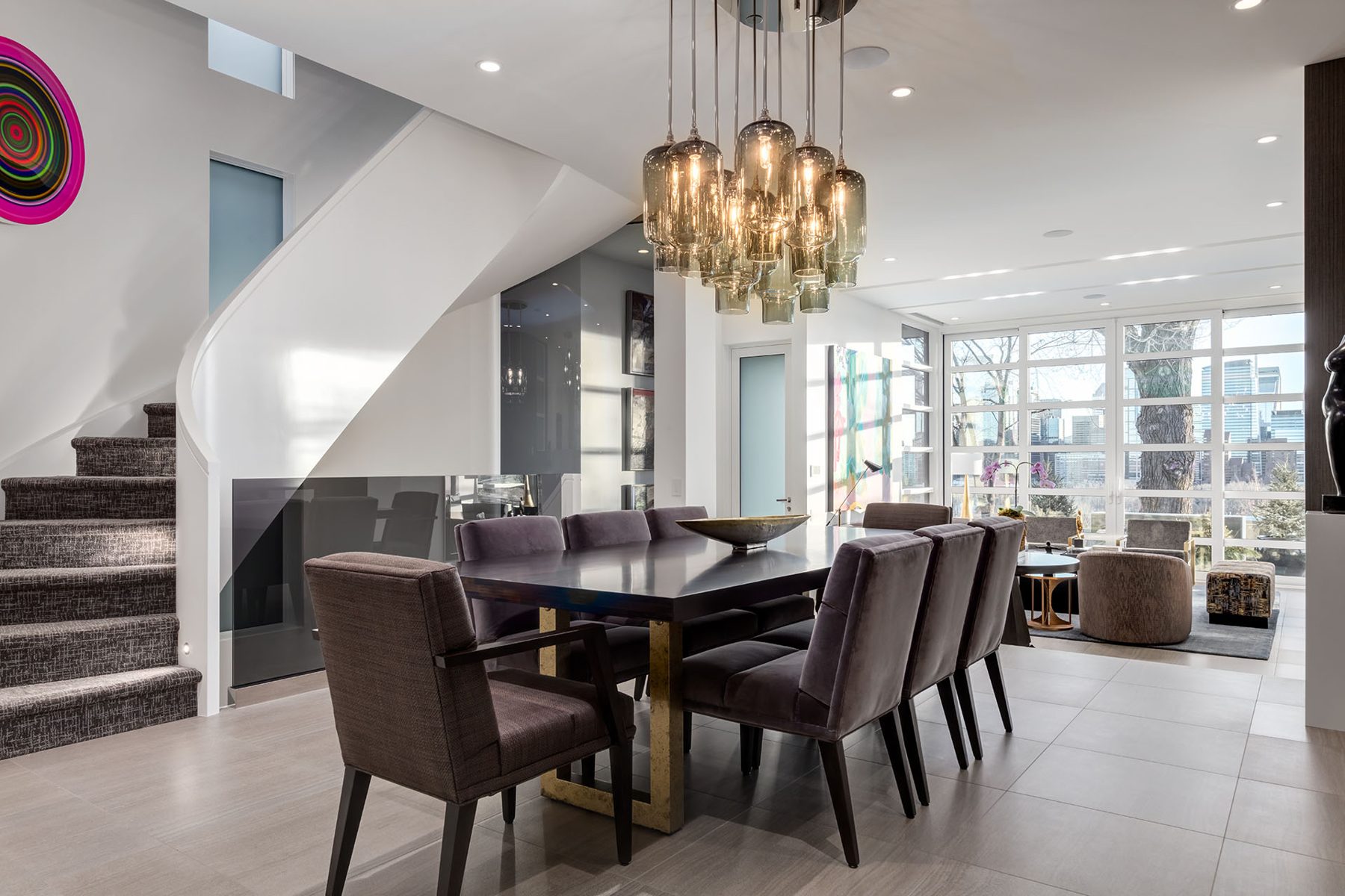 Modern dining room with glass staircase, plush chairs, and large windows — Skyline