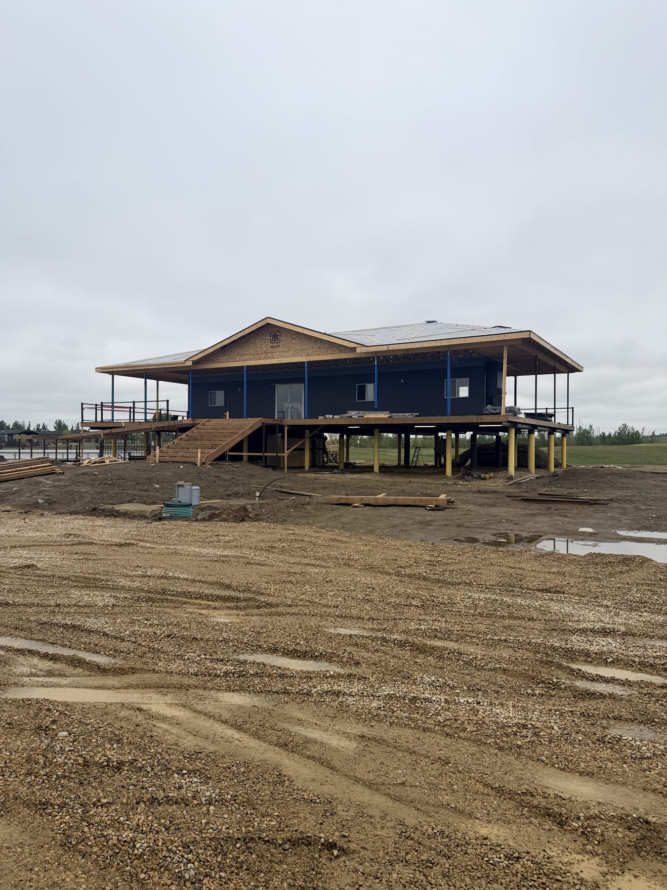 Elevated house construction with wood framing and dark siding visible — Sandy Point (Club House)