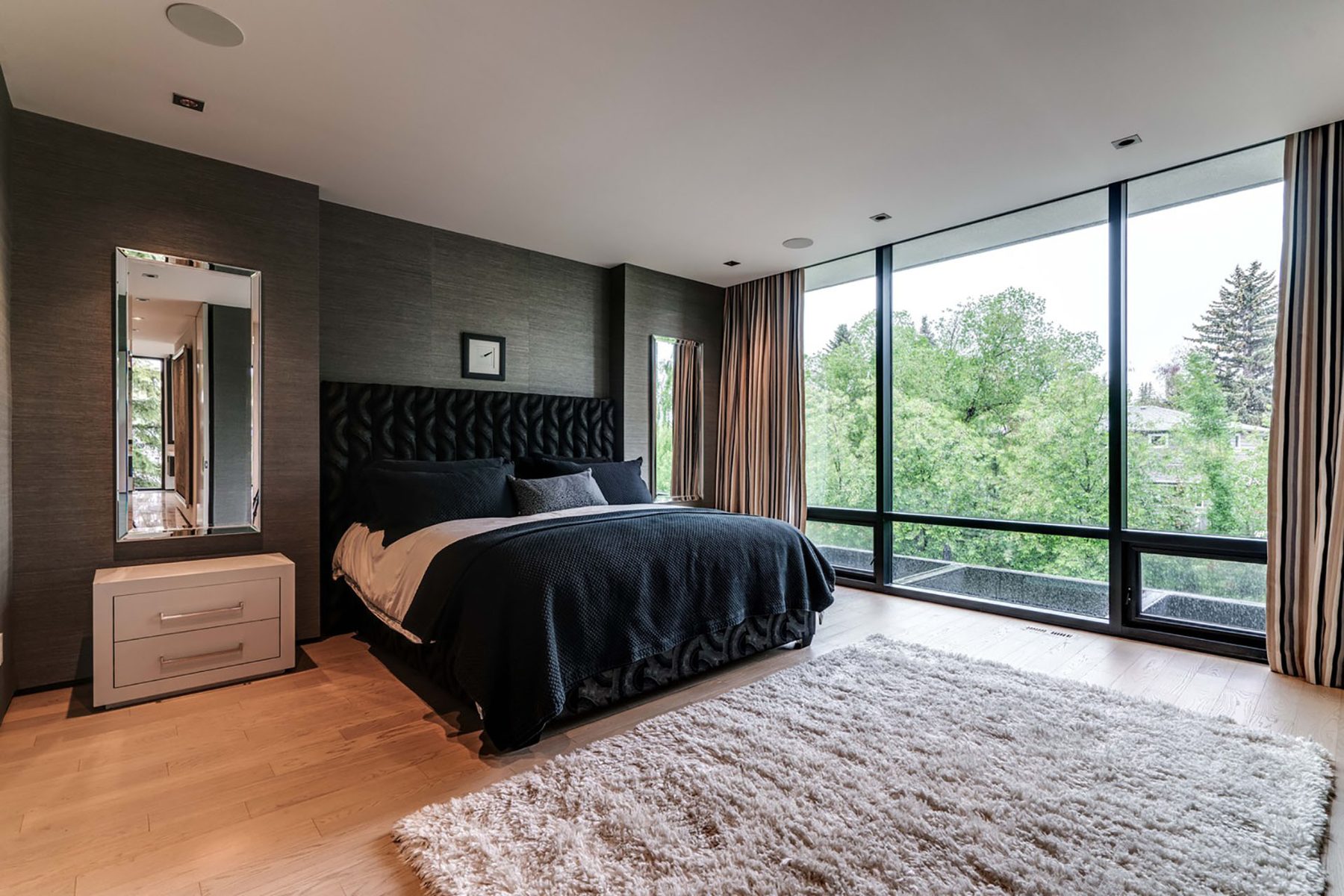 Modern bedroom with large windows, dark walls, wood floor, and plush rug — Modern Family
