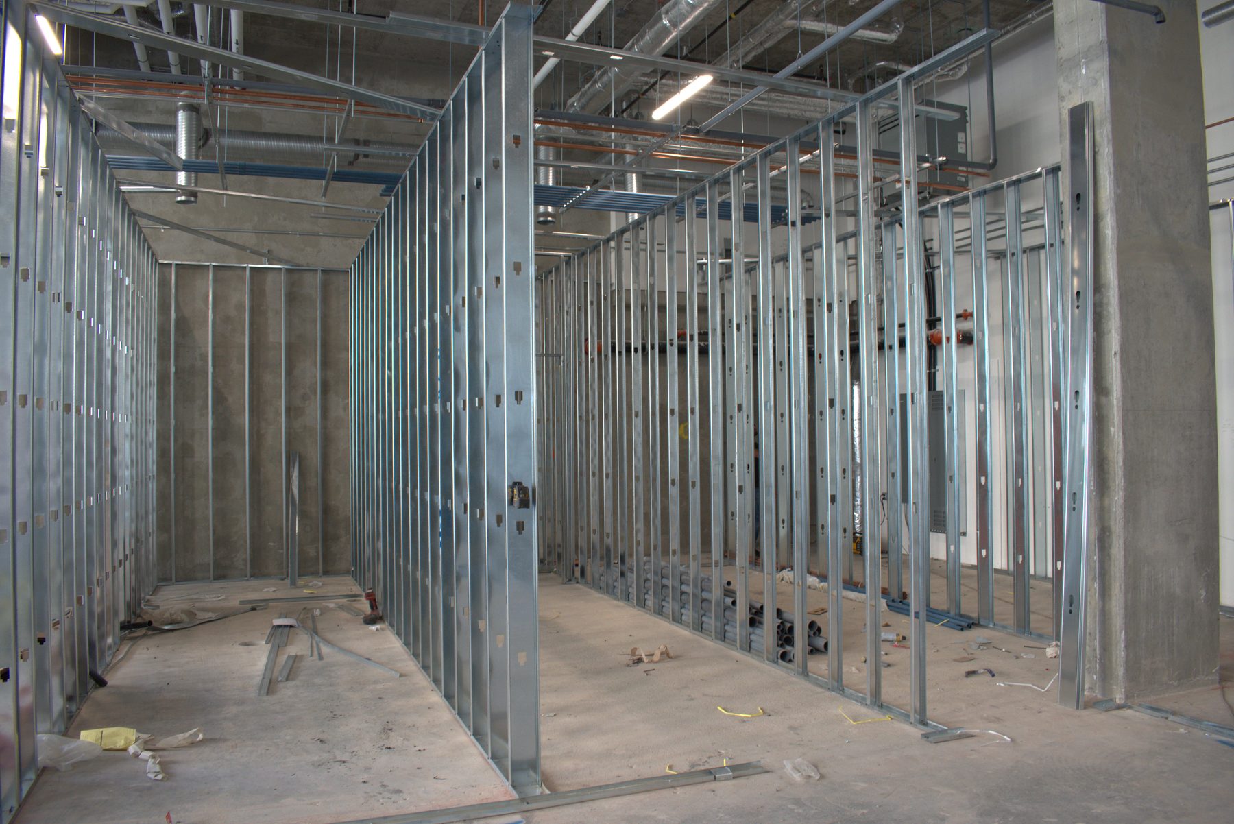 Metal studs frame interior walls with exposed conduit and pipes above — Leela Spa (West District)