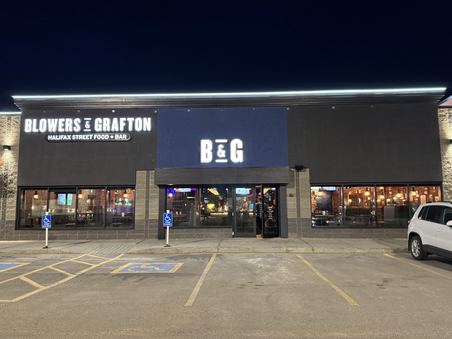 Storefront facade with illuminated signs and parking lot at night — Blowers and Grafton (Lloydminster)